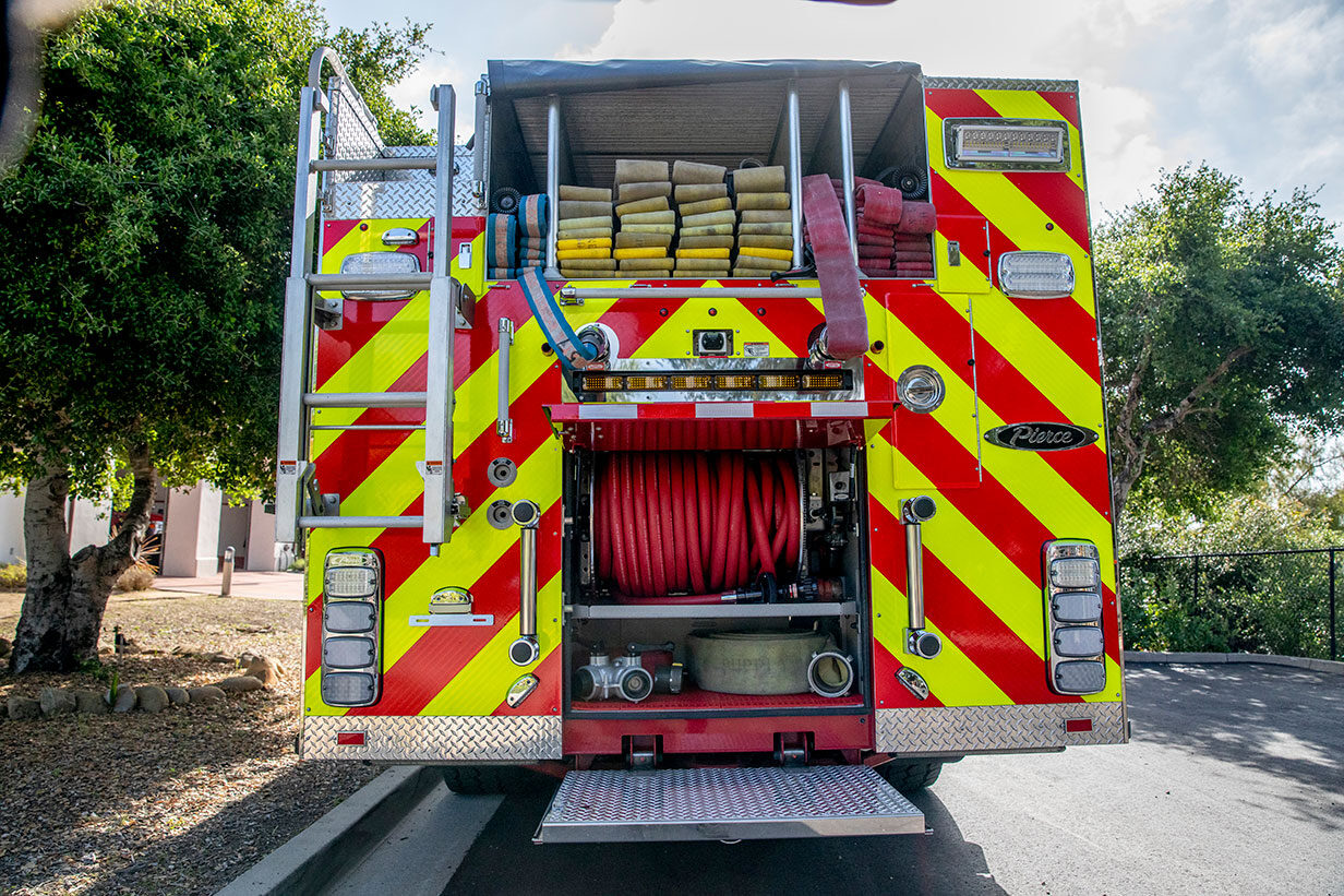 The rear of a fire truck with the compartments open showing hose in the hosebed and a booster reel.