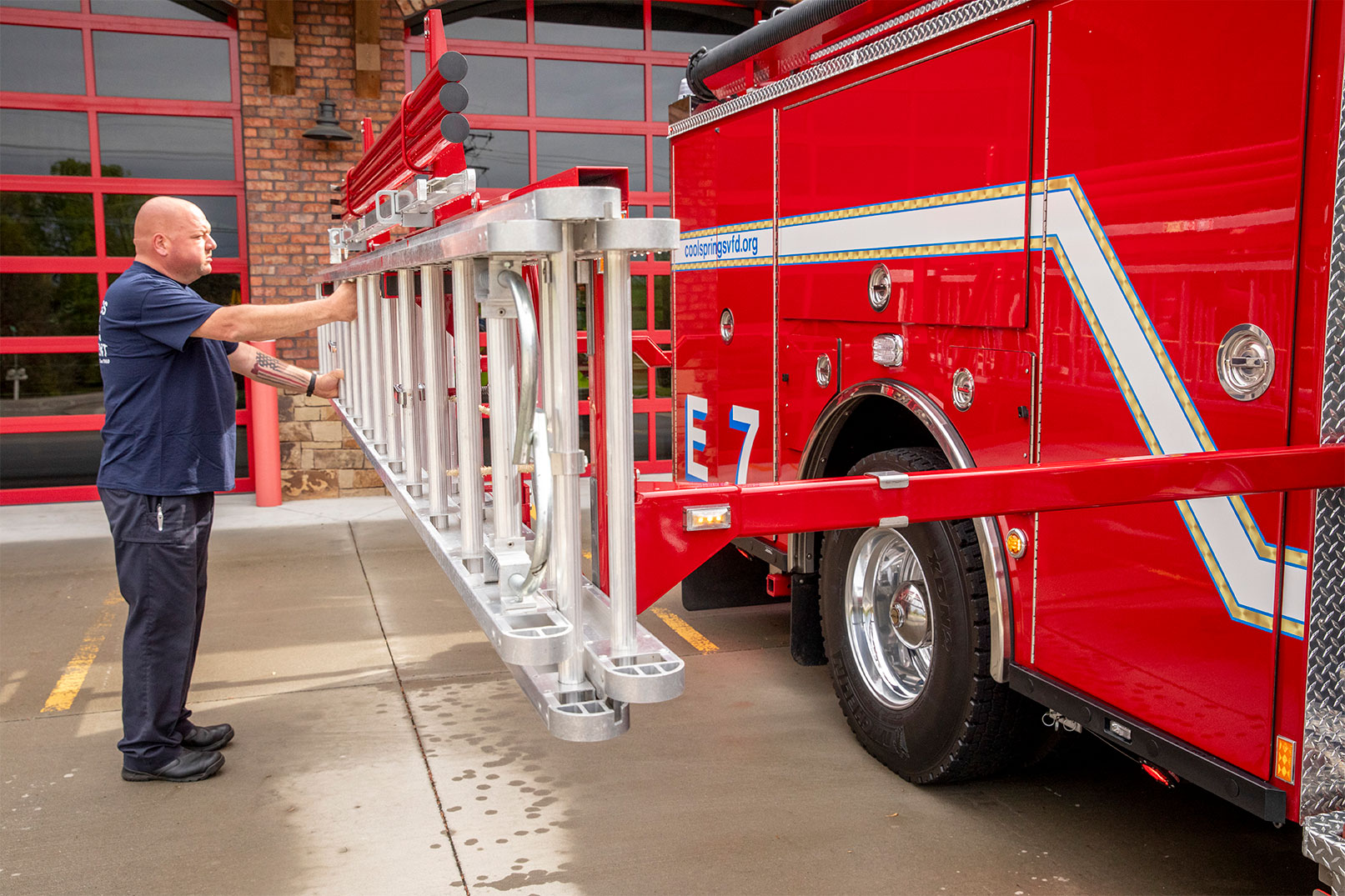 A firefighter grabbing ground ladders from the hydraulic lader rack on the officers side of a fire truck.