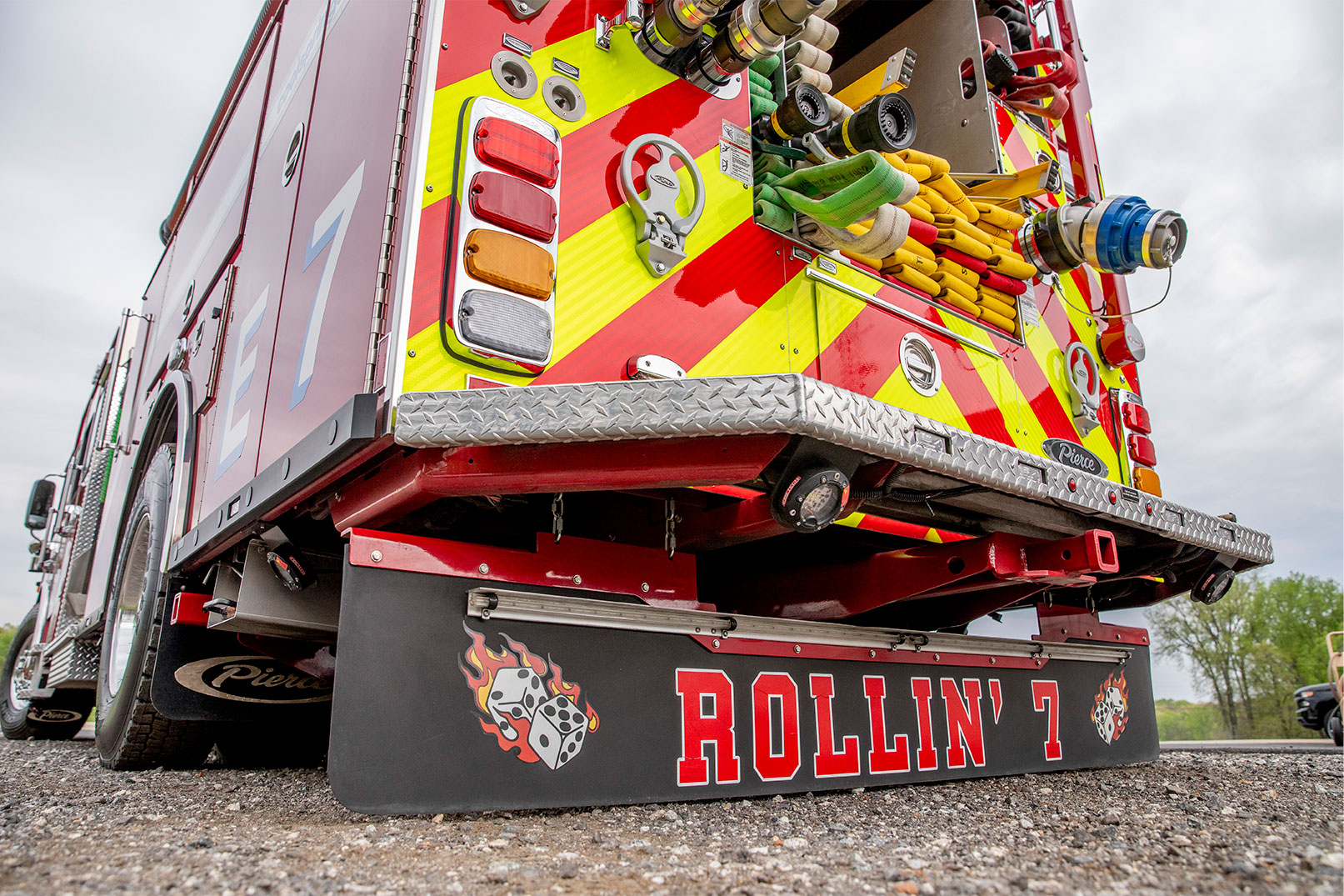 The rear drivers side of a fire truck with hose in the hosebed and a graphic on the mudflap behind the rear set of tires.