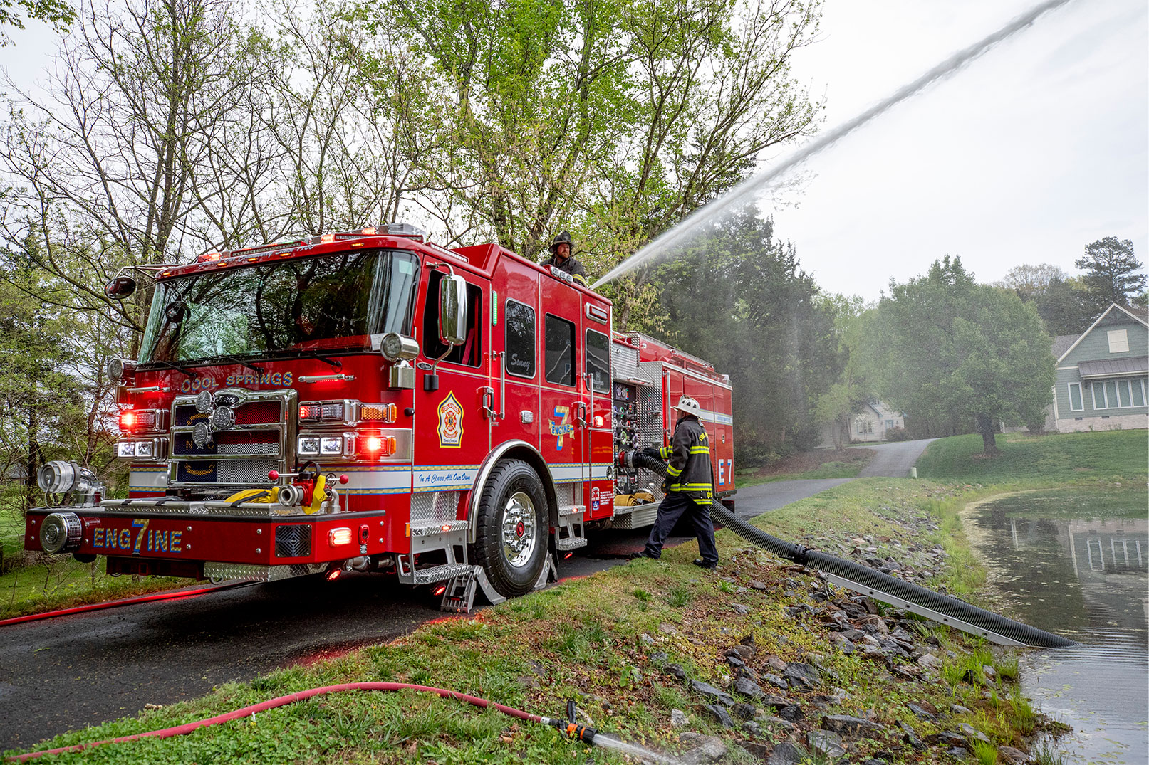 Two firefighters operating a fire truck by using water from a pond and spraying water from the deck gun on top of the pumper.