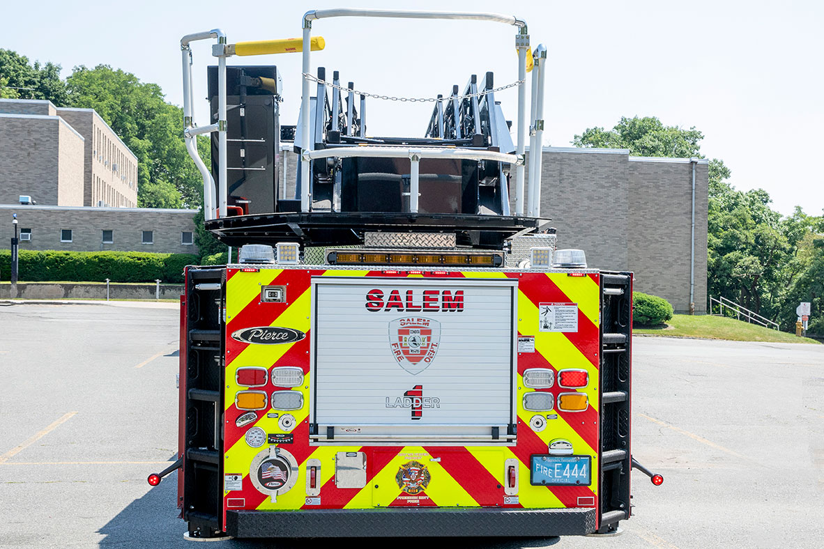 The rear of an aerial ladder fire truck in a parking lot on a sunny day.