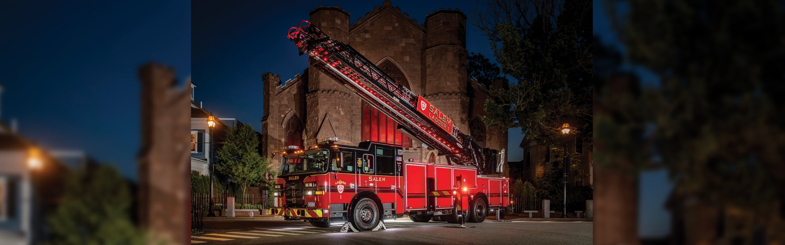 A 100' Heavy-Duty Low Profile Steel Aerial Ladder in front of a brick building at night with red lights.