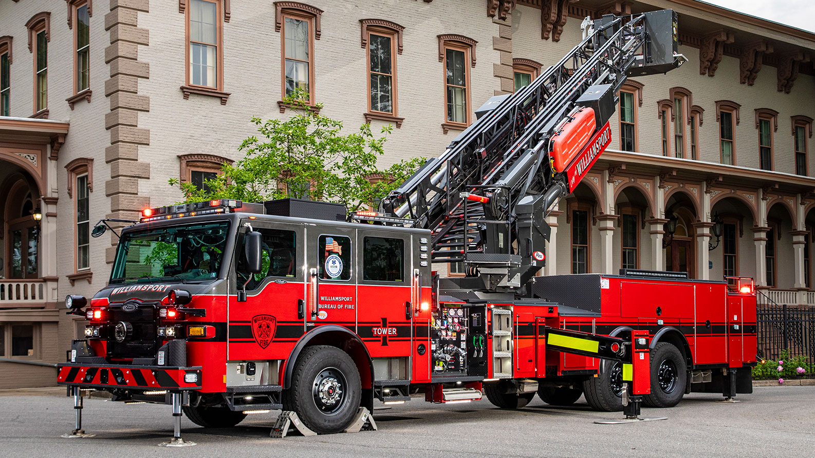 The front driver's side of a Velocity 100 Ascendant Aerial Tower with the lights on with the aerial up next to a brick building.