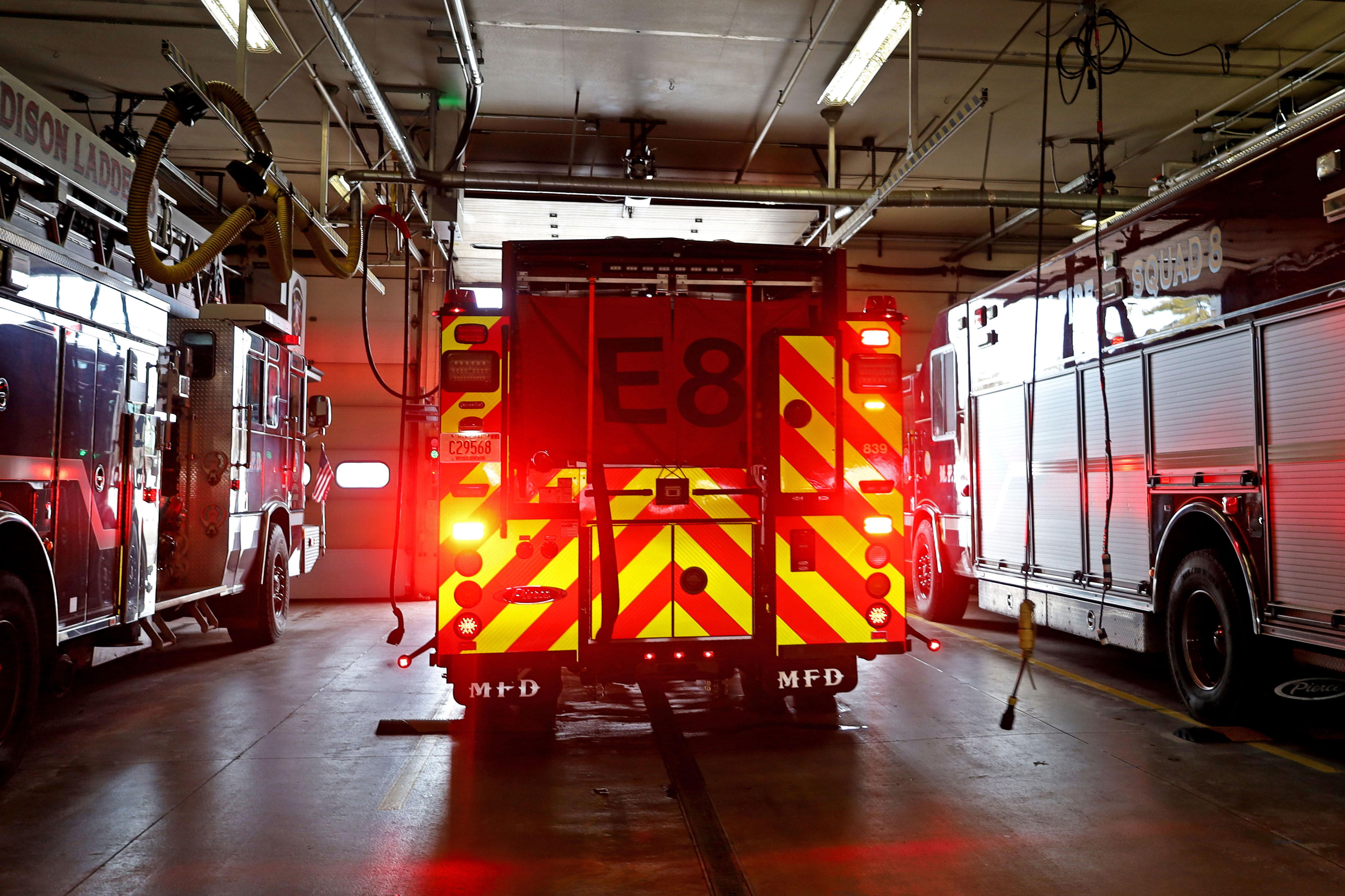An electric fire truck is pulling out of a fire station bay with red lights visible with a red and yellow chevron pattern.
