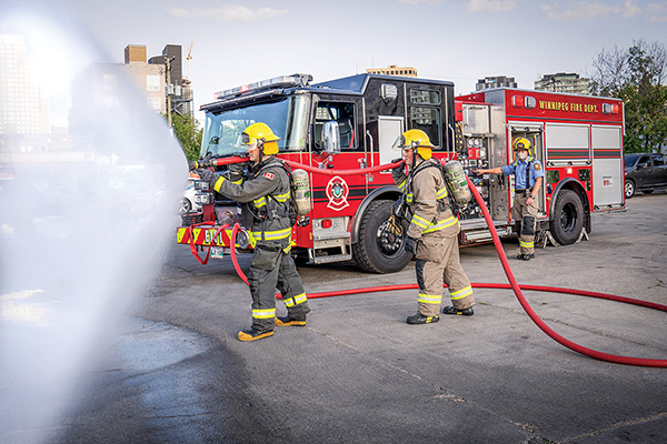 Winnipeg Canada Fire Department members spraying water from hose next to their Pierce pumper fire truck