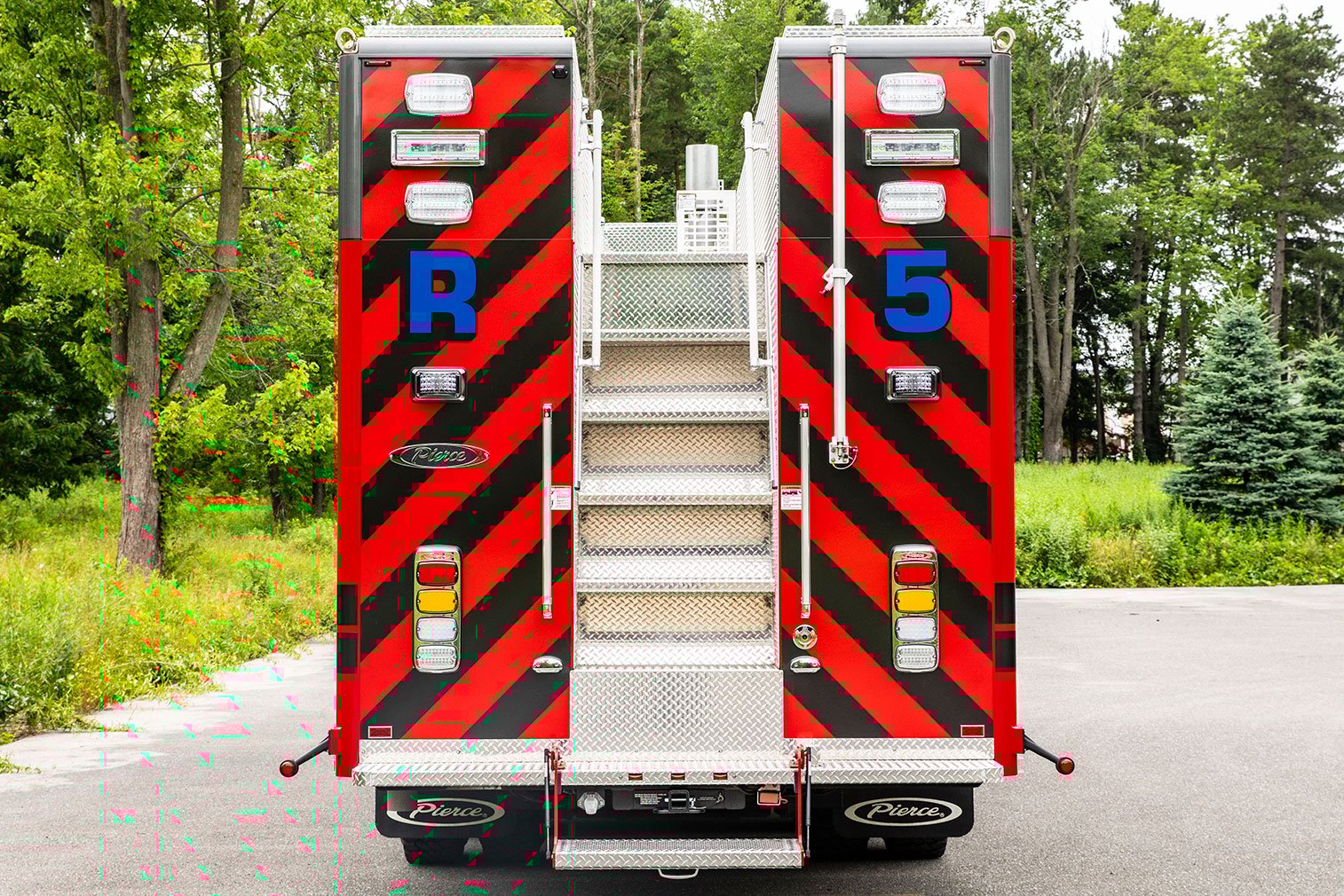 The rear of a HDR with steps in the center leading to the top and chevron graphics on the back parked beside a wooded area.