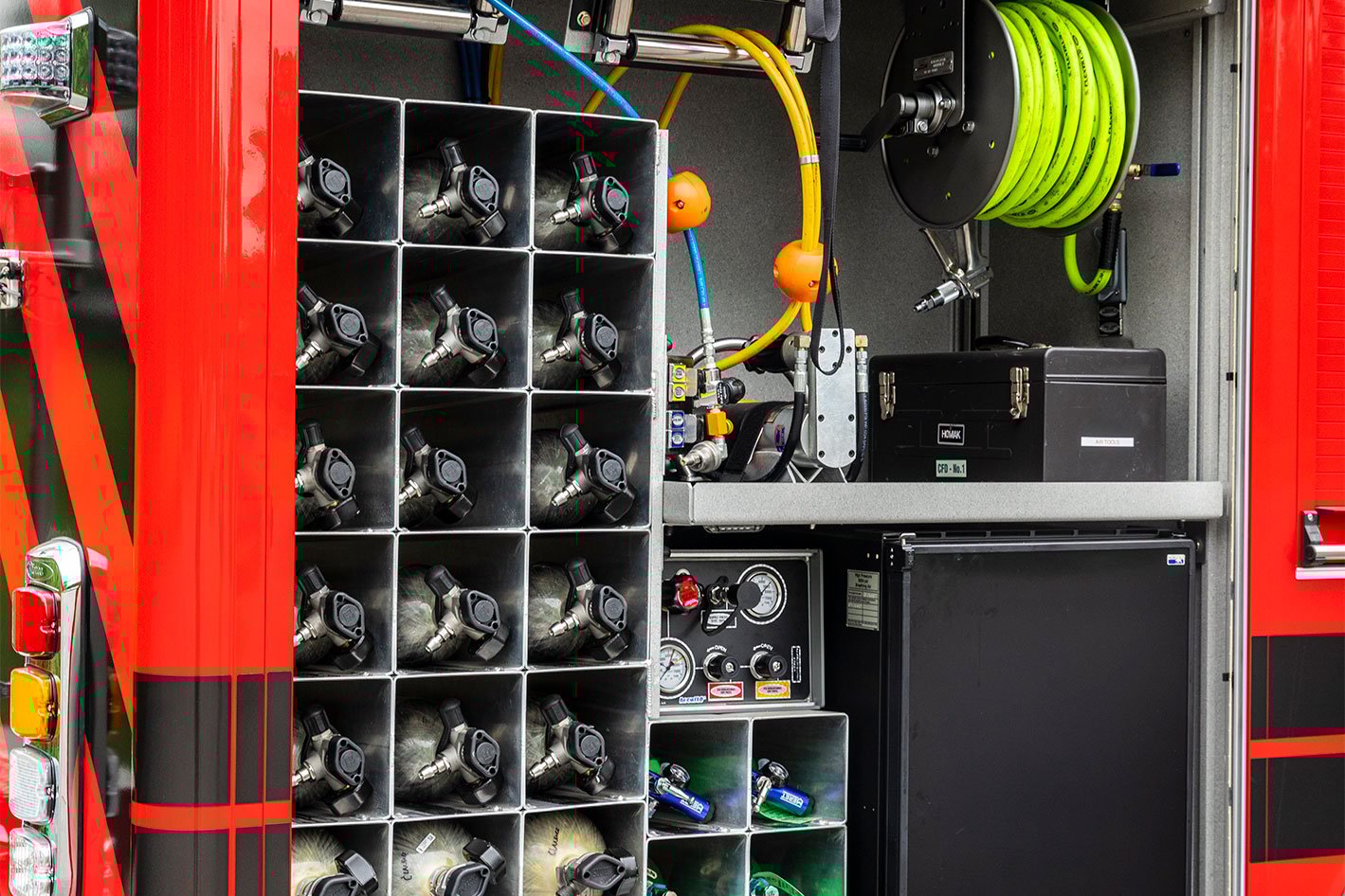 The rear officer's side compartment of a rescue fire truck with the rollup door open showing air bottles, a fridge and hose and cord reels.