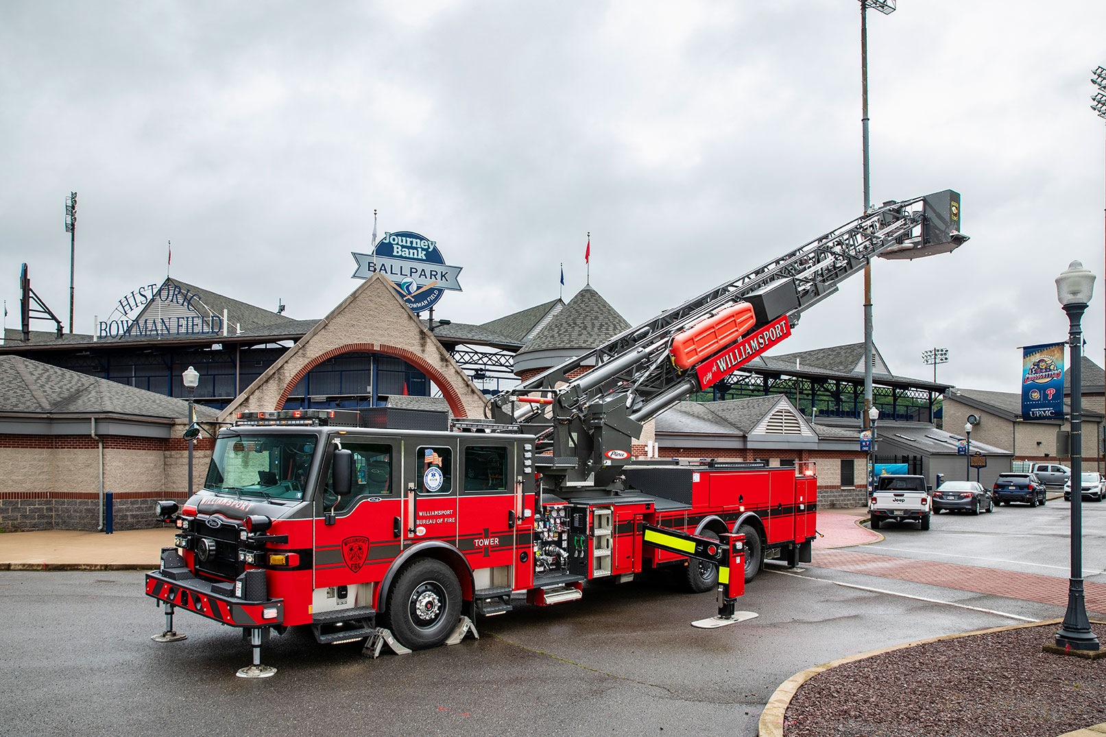 The front driver's side of a Velocity 100' Ascendant Aerial Ladder with the aerial up parked in front of a baseball stadium.