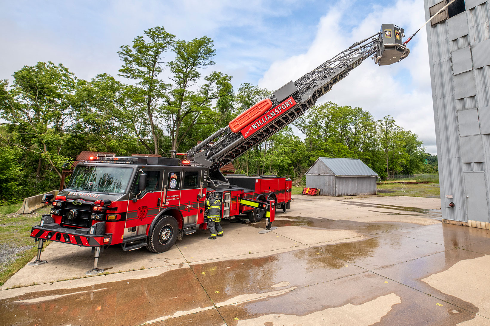 The front driver's side of a Velocity 100' Ascendant Aerial Tower with the aerail extended to a firefighter training center building.