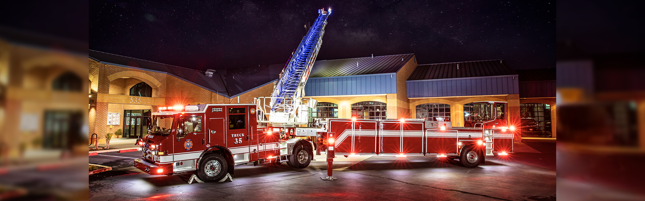 The driver's side of a Velocity Ascendant 107' Heavy-Duty Tractor Drawn Aerial with the lights at a fire station.