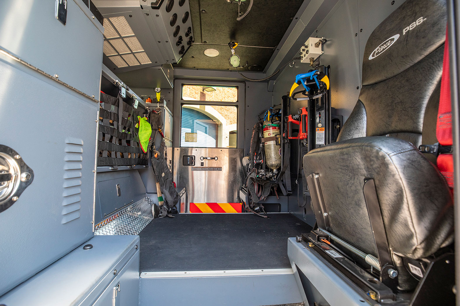 The inside of a fire truck crew cab with gear and tools in the compartments and a seat for a firefighter.
