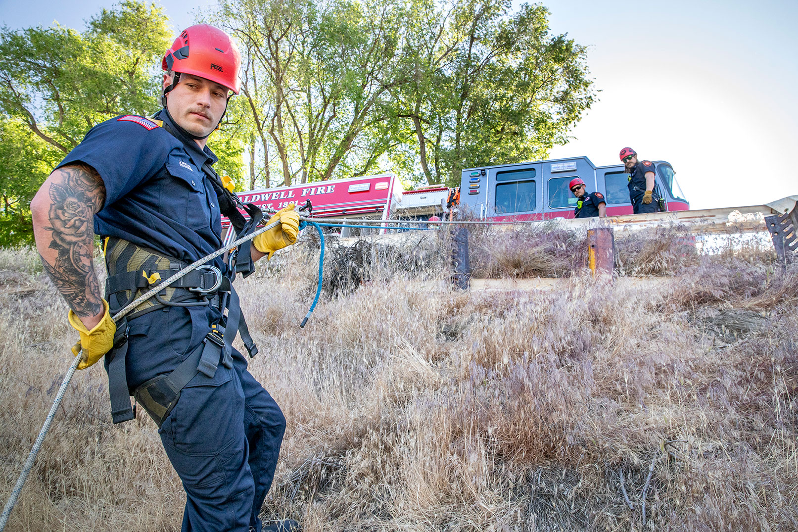 A firefighter in a harness and helmet repelling with ropes down a cliff from a fire truck.