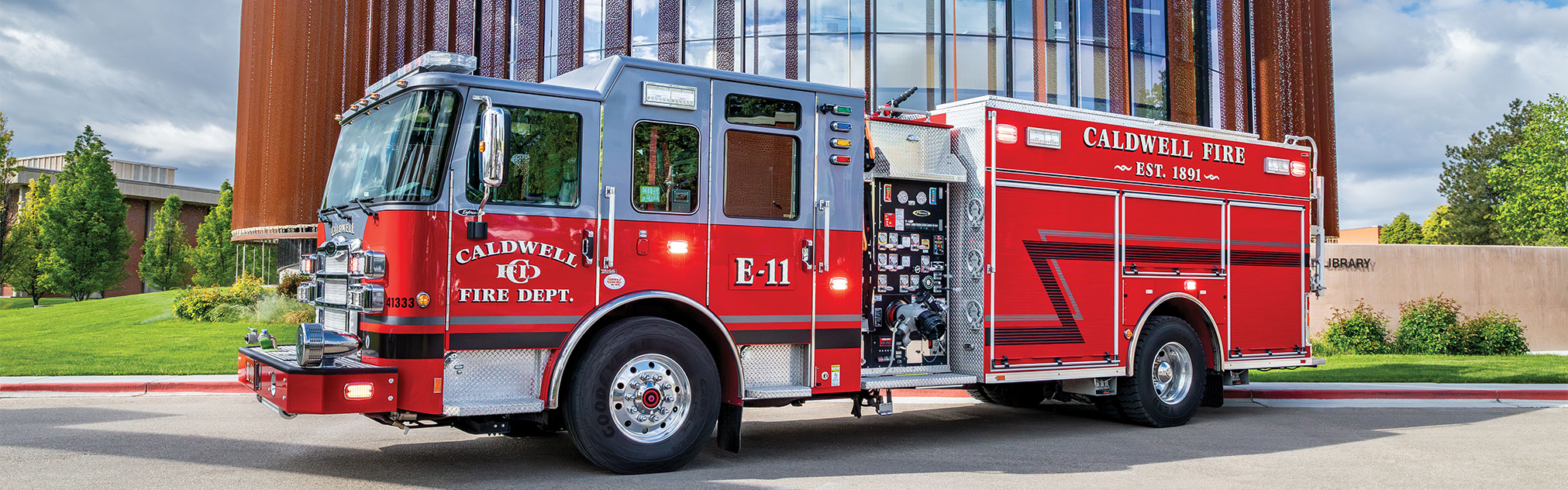 The driver's side of an Enforcer Heavy-Duty Rescue Pumper parked in front of a large building on a sunny day.
