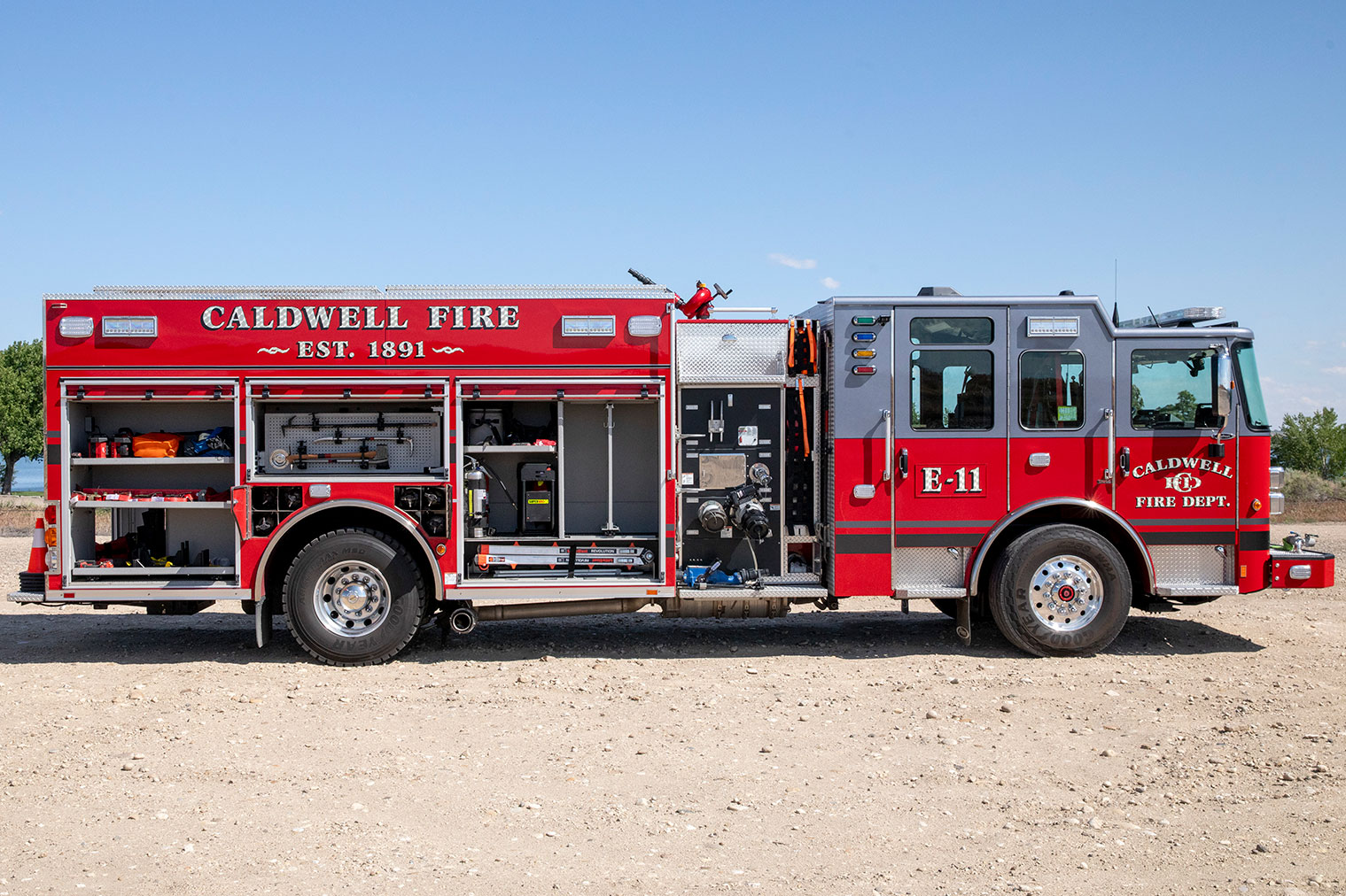 The officers side of an Enforcer Heavy-Duty Rescue Pumper with the compartments open showing tools and equipment inside.