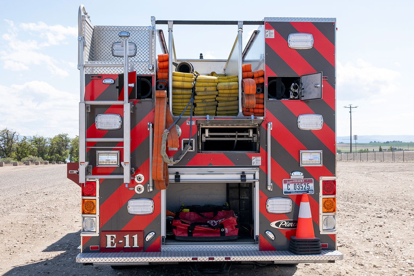 The rear of a fire truck with the compartments open, the hosebed loaded and traffic cones on the rear bumper.