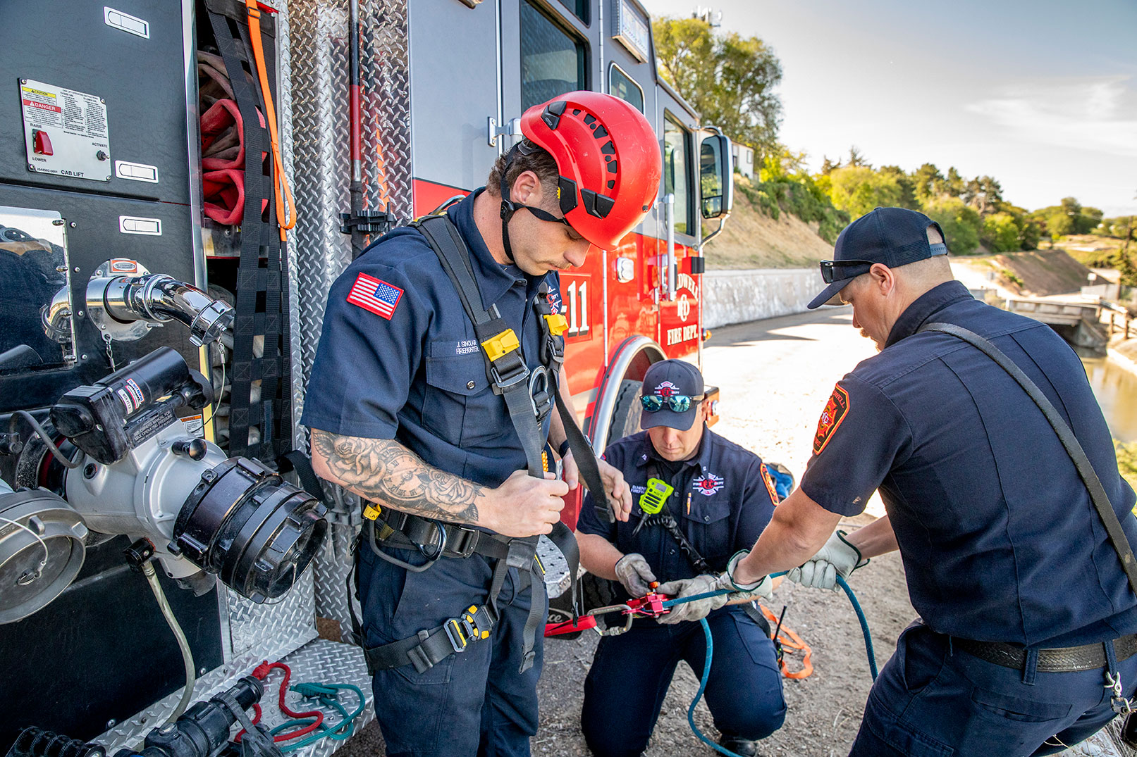 Two firefighters helping rig another firefighter up in a harness for a rope rescue.