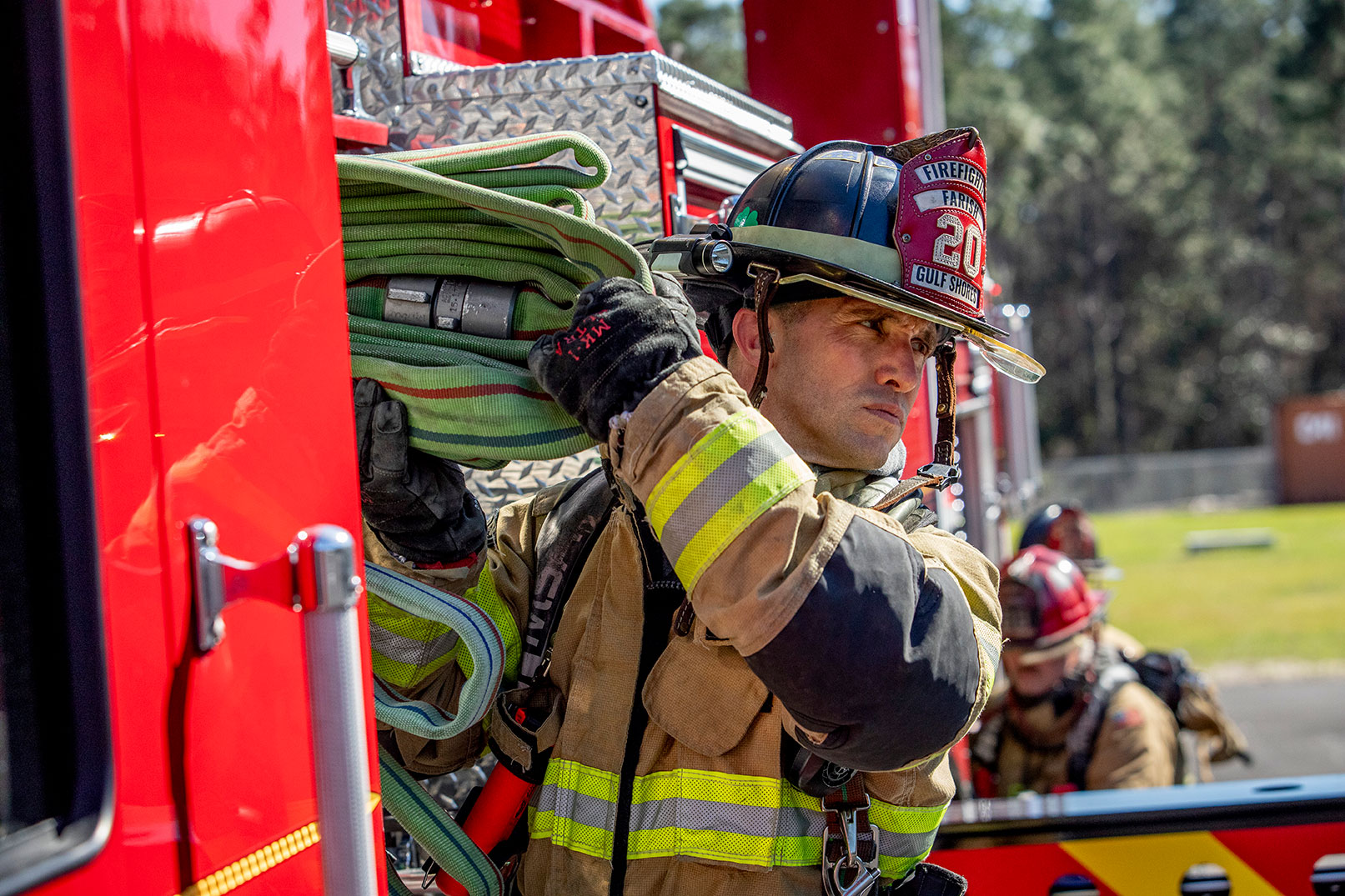 A firefighter in turnout gear pulling green hose from the crosslays of a fire truck.