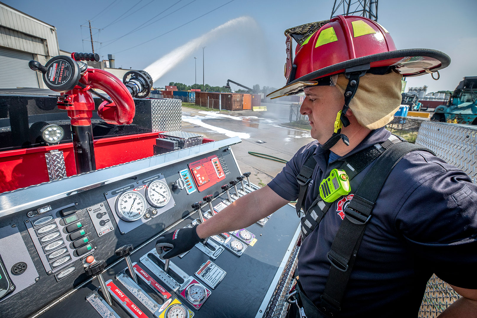 A firefighter operating a top mount pump panel on a fire truck using levers and guages to spray water.