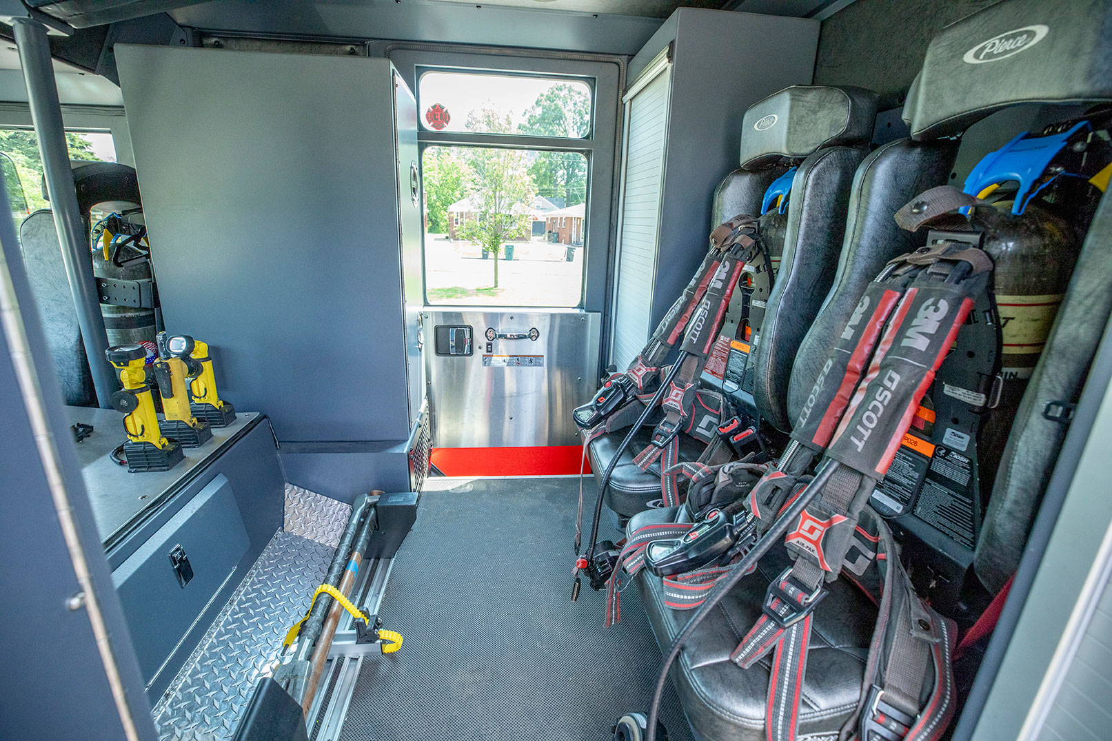 The crew cab of a fire truck with two forward facing seats with SCBAs and rollup door compartments.
