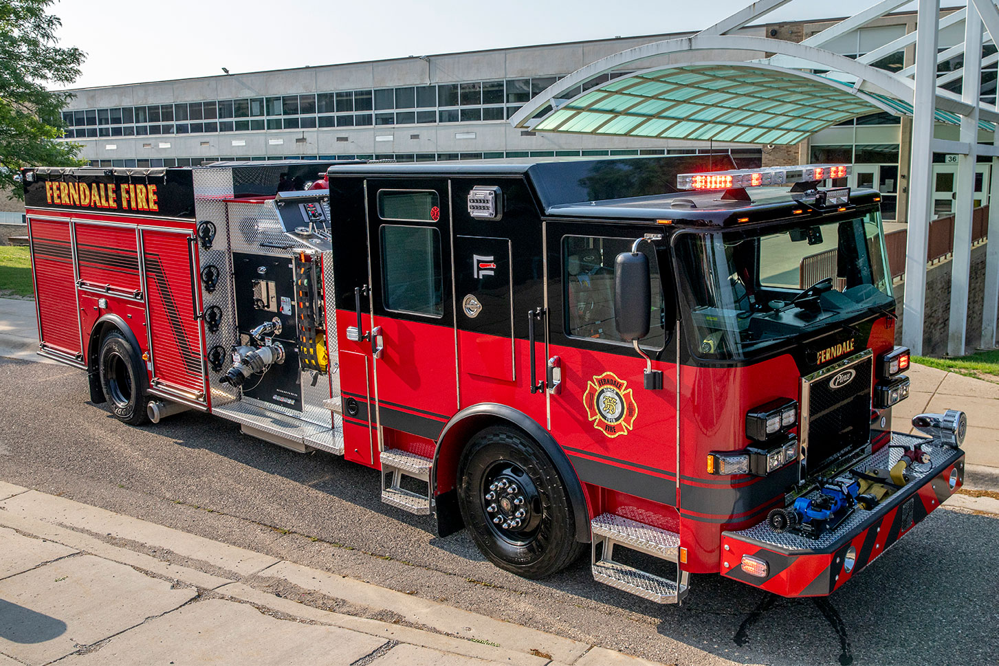 The front drivers side of a Saber Pumper driving on a narrow one way street by a big glass and concrete building.