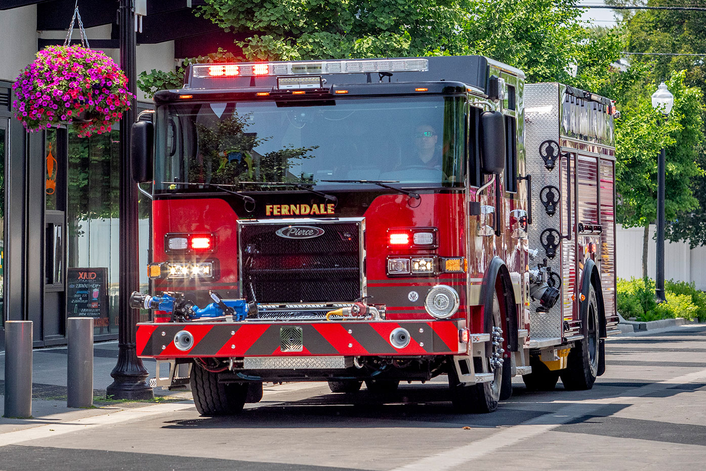 The front drivers side of a Saber Pumper fire truck driving on a city street with landscaping.