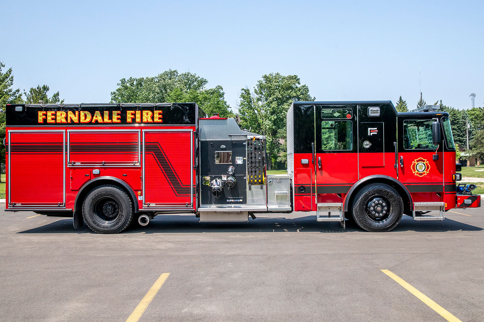 The officers side of a Saber Pumper fire truck in a parking lot on a sunny day with no clouds in the sky.