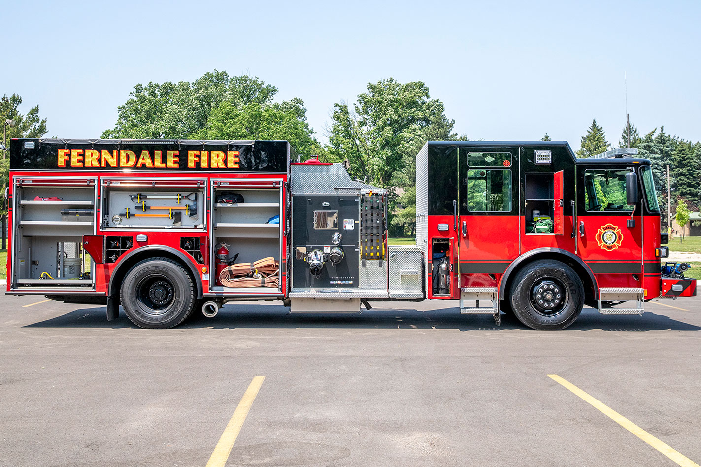 The officers side of a Saber Top-Mount Pumper fire truck with the compartments open showing equipment and tools.