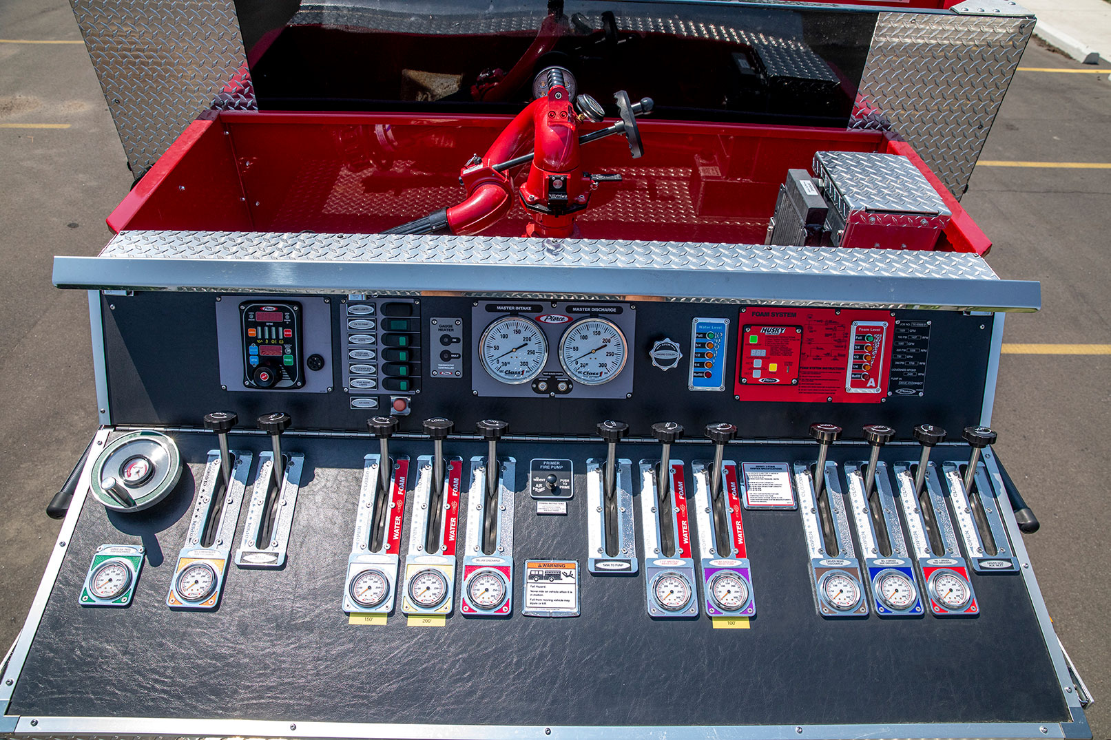 The top over of top-mounted pump panel of a fire truck with levers, gauges and a foam system.