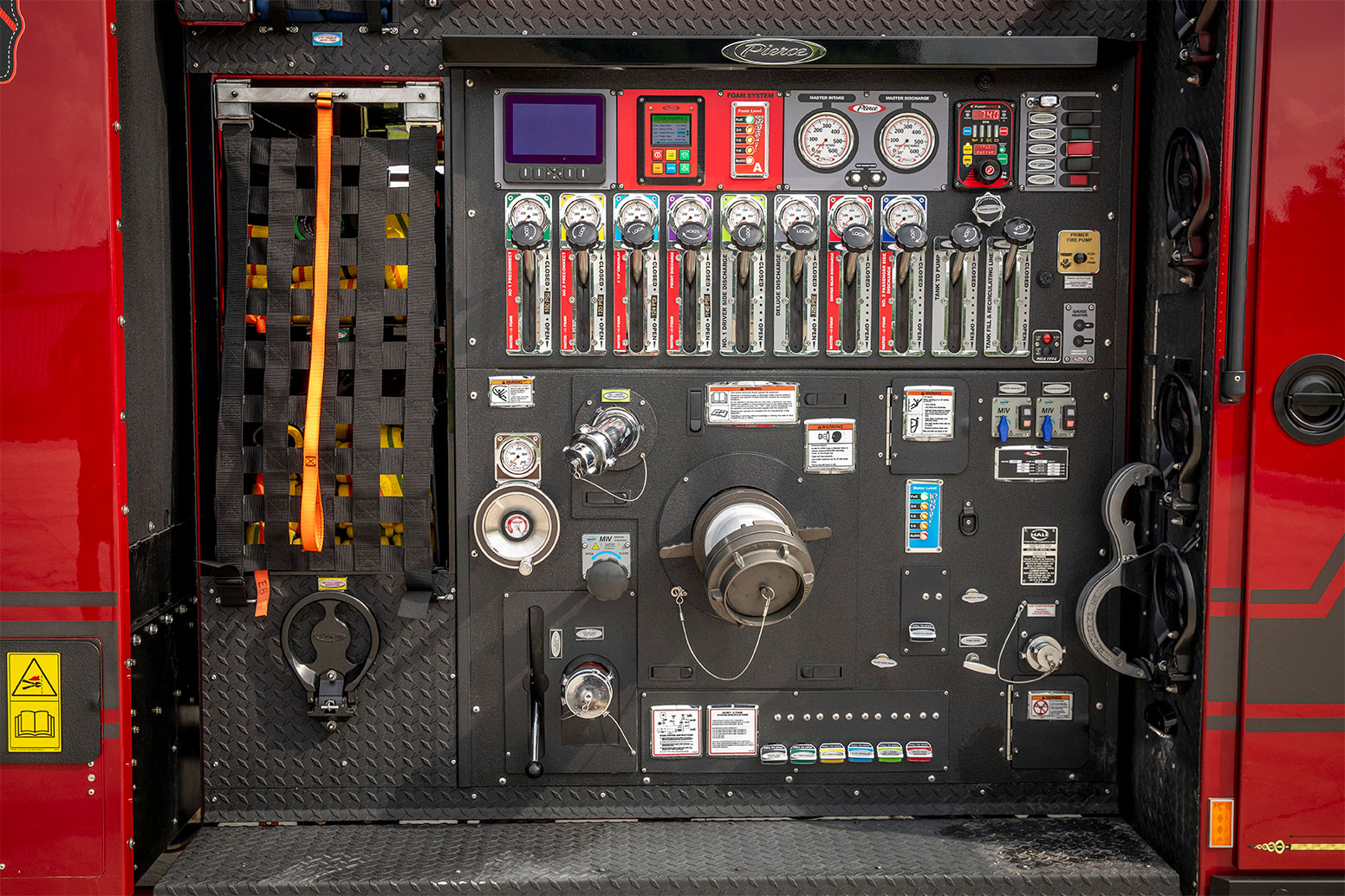 The hosebed of an electric fire truck with levers and guages beside crosslays with hose.