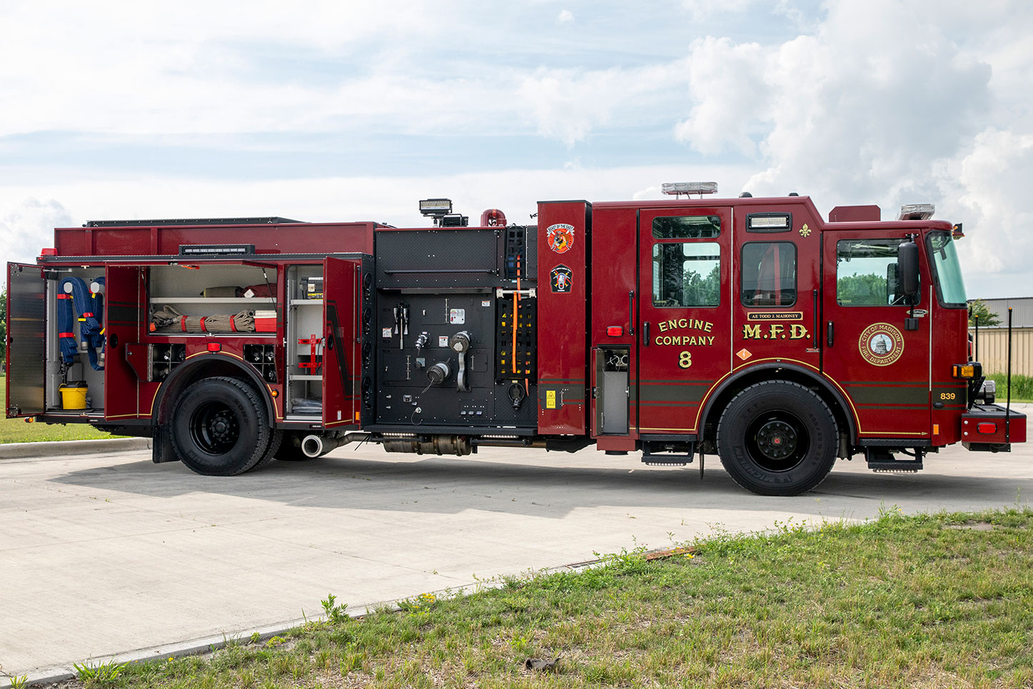 The officers side of an Enforcer Volterra Electric Fire Truck in a parking lot with the compartments open showing equipment inside.