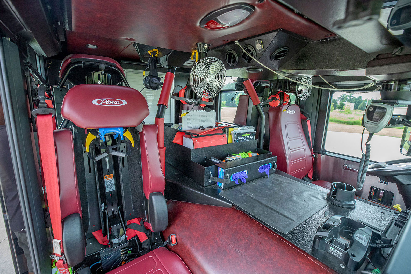 The inside of an EV fire truck with red vinyl interior and compartments holding maps and rubber gloves for firefighters.