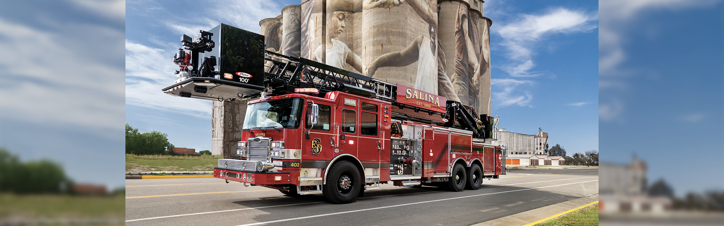 The front driver's side of an Enforcer 100’ Heavy-Duty Steel Aerial Platform driving on a road in front of a historic building.