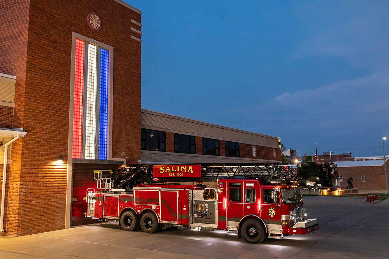 The officers side of an Enforcer 100 Aerial Platform with the lights on parked in front of a brick fire house.