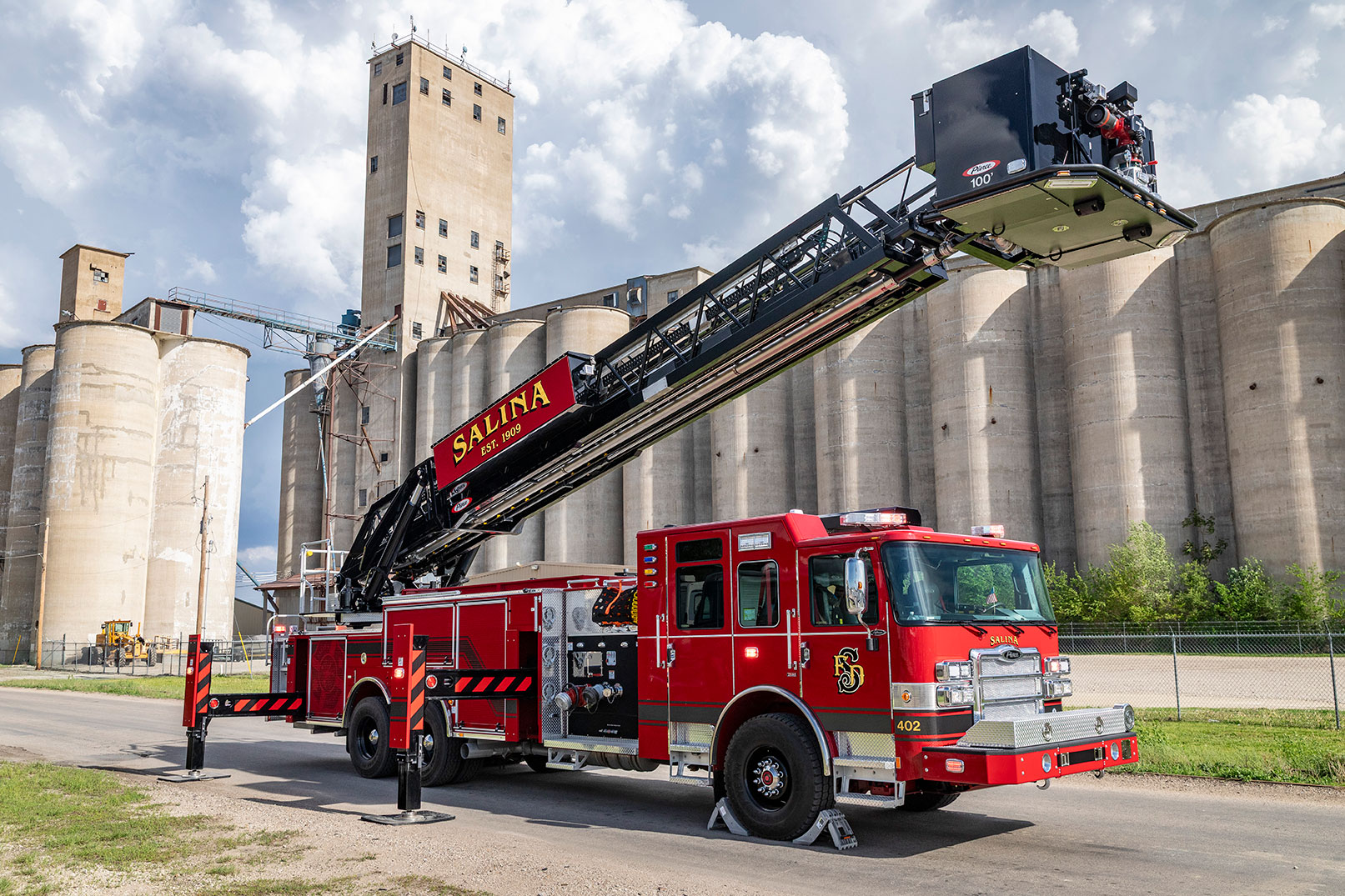 The officer's side of an Enforcer 100' Heavy-Duty Aerial Platform parked in front of a concrete building with the aerial up.