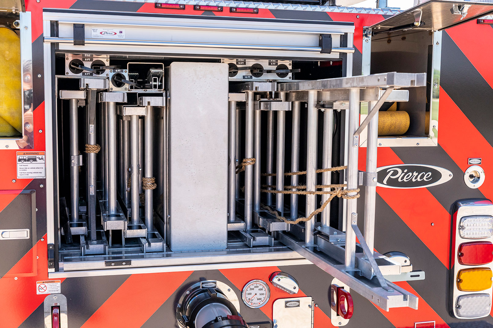 The rear of a fire truck with the compartments open showing ground ladders and hose.