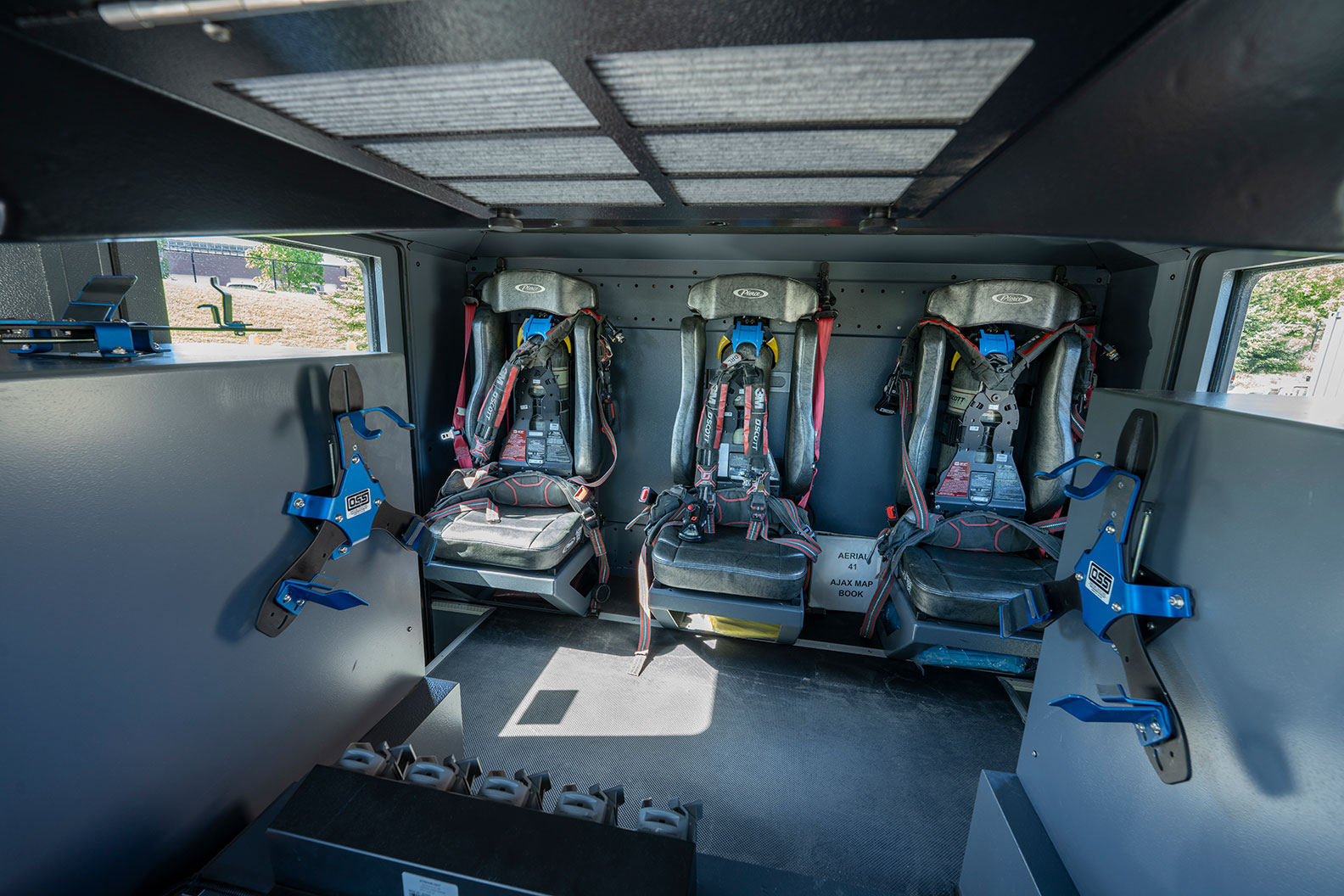 The crew cab of a fire truck with three seats including SCBA holders for firefighters and compartments for equipment.