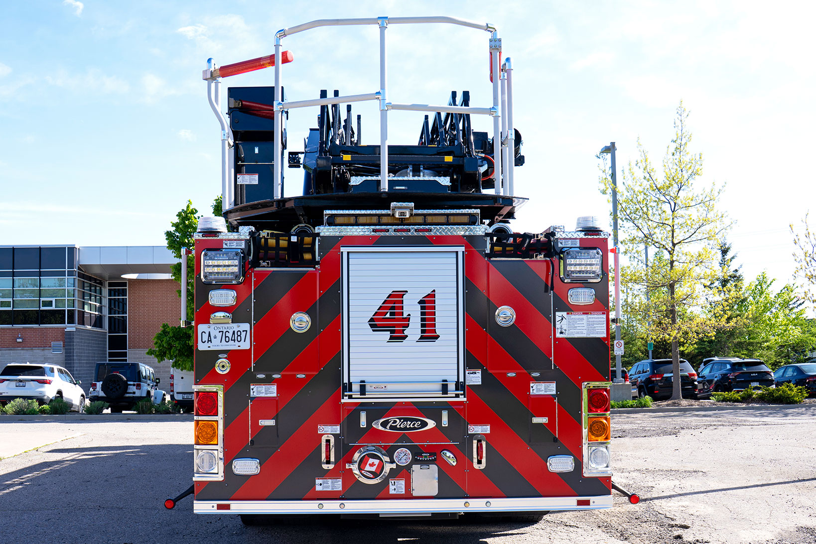 The rear of an aerial fire truck with a red and black chevron pattern in a parking lot on a mostly sunny day.