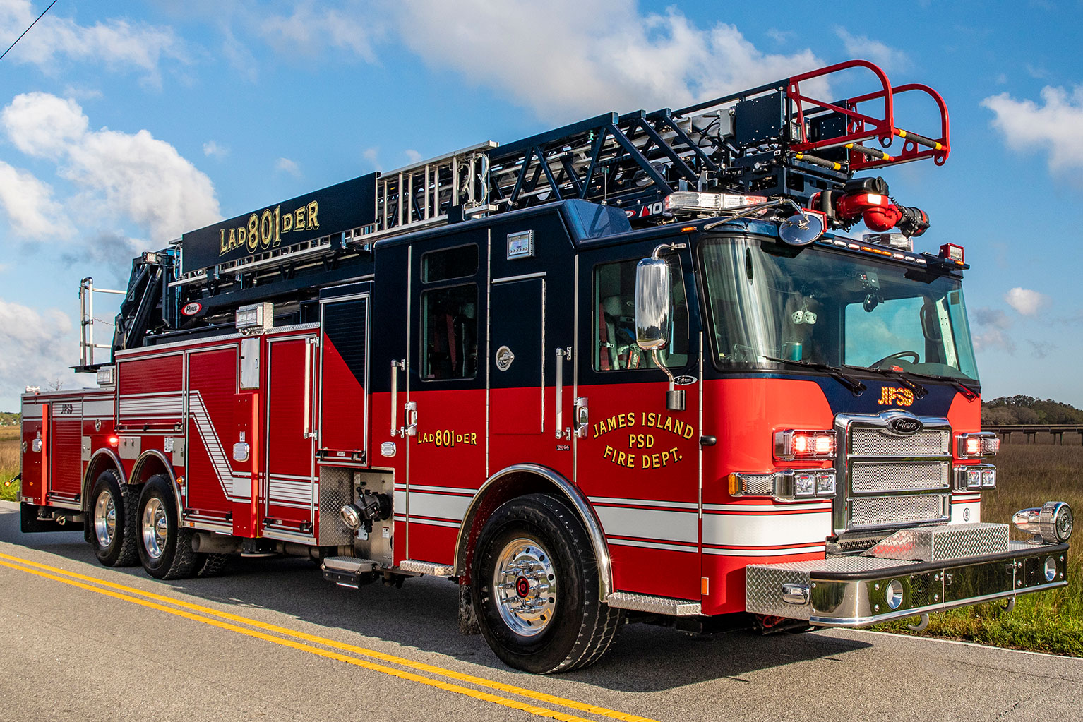 The front drivers side of an Enforcer 107 Ascendant Aerial Ladder parked on a two lane road in front of a marsh.