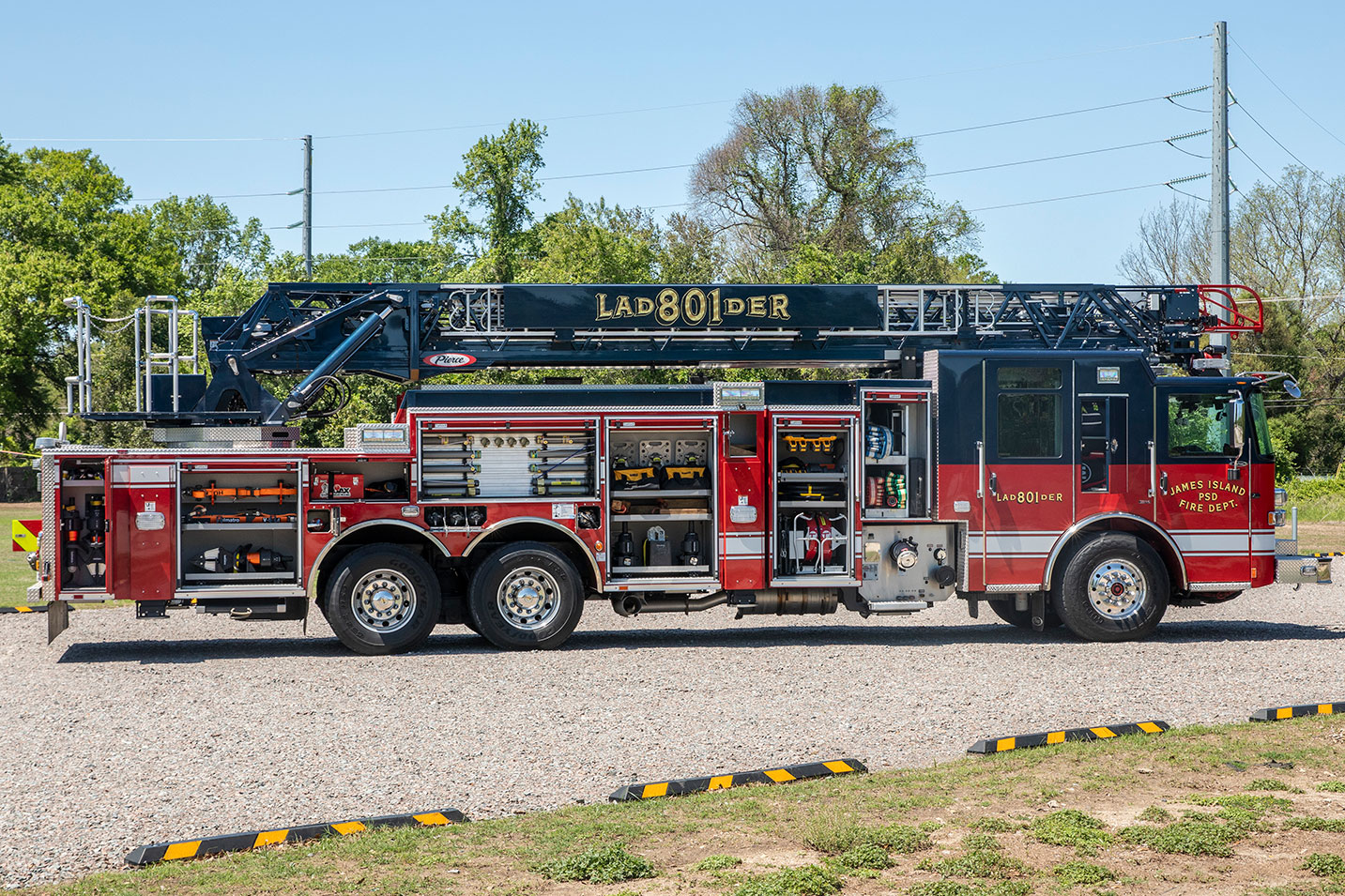 The officers side of an Enforcer 107 Ascendant Aerial Ladder with the compartments open showing tools and equipment inside.