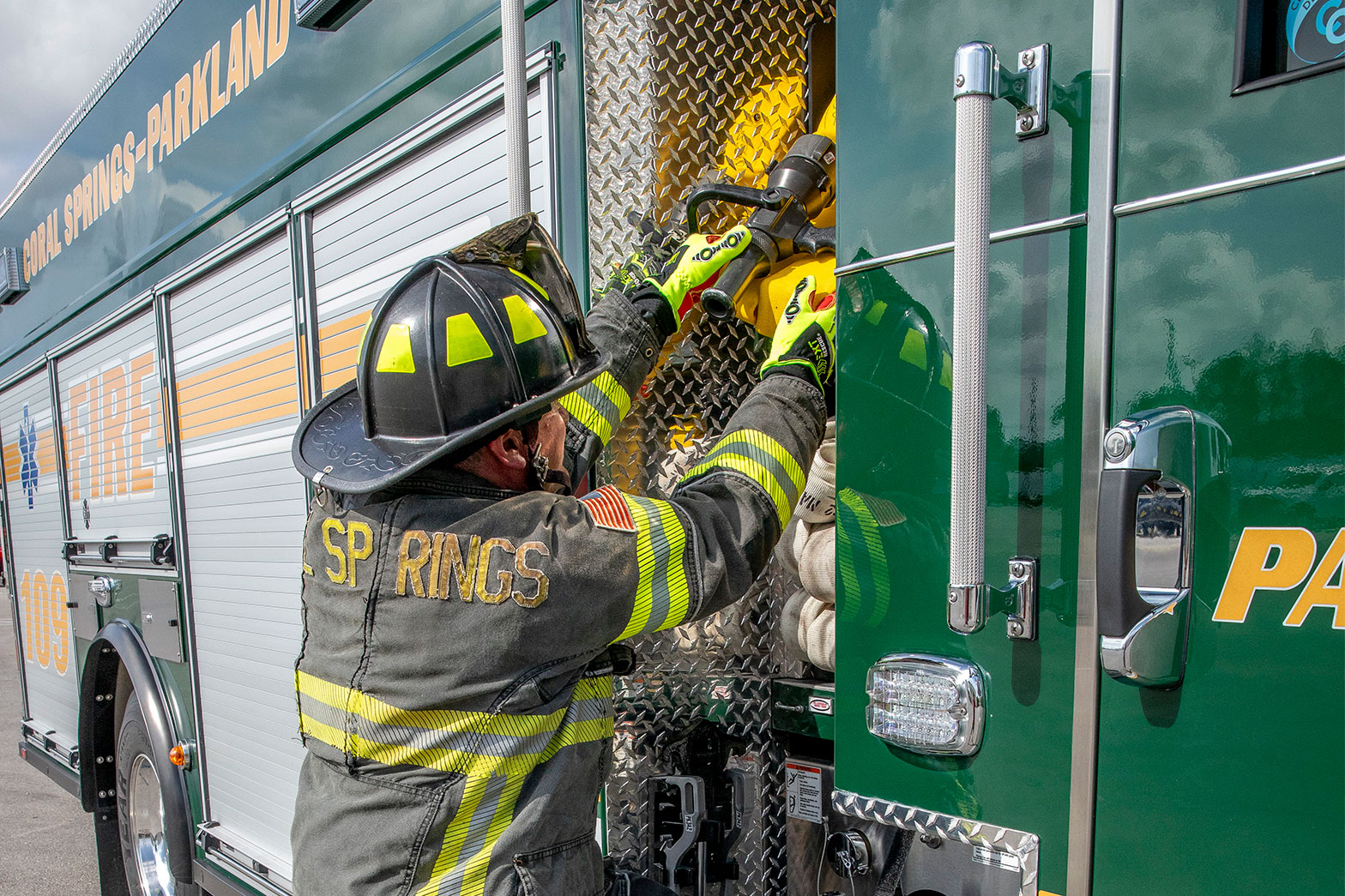 A firefighter in turnout gear pulling fire hose from the crosslays of a Pumper fire truck.
