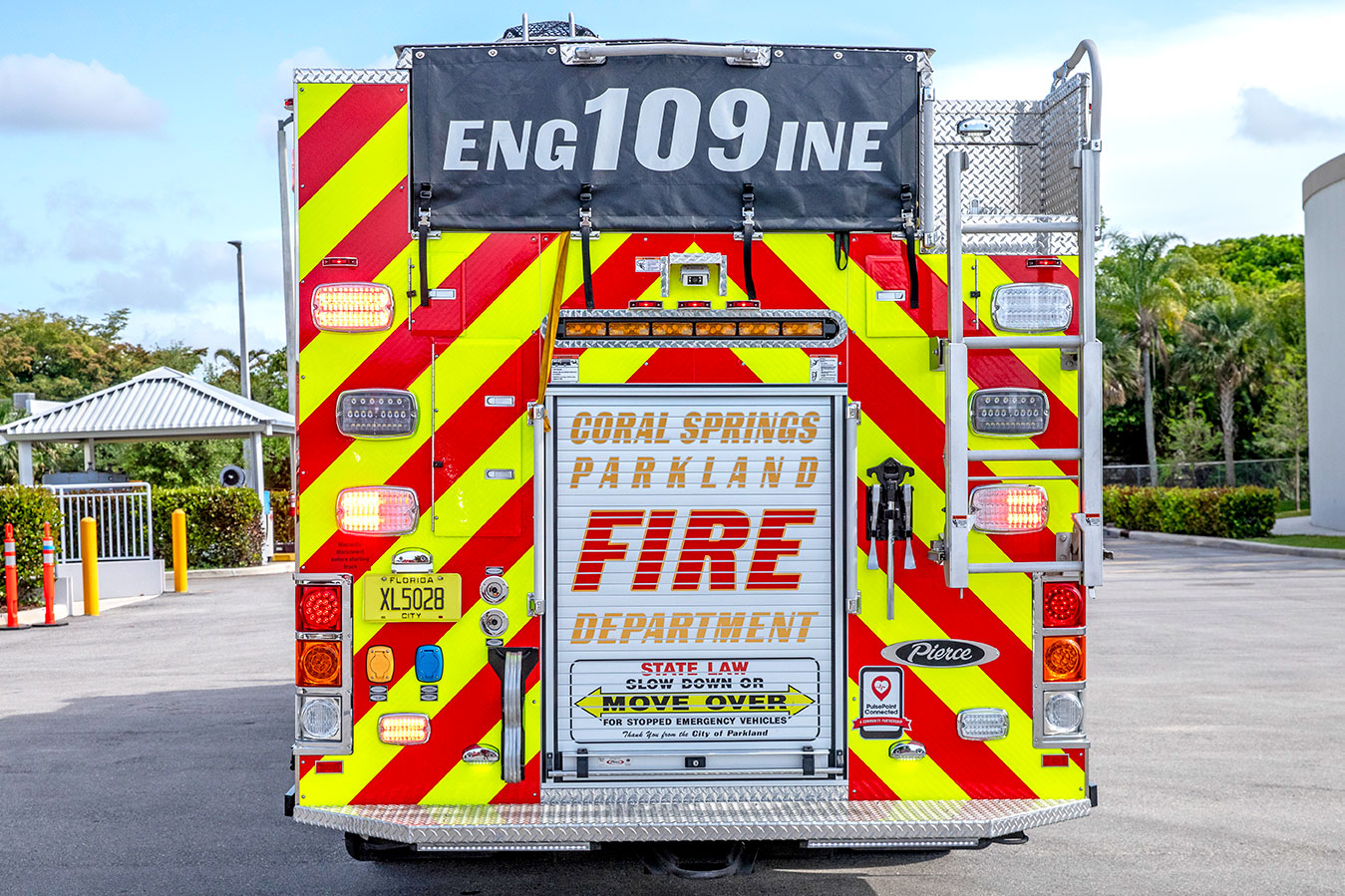 The rear of a pumper fire truck with a chevron patter and graphics on the hosebed cover and compartment door in a parking lot.