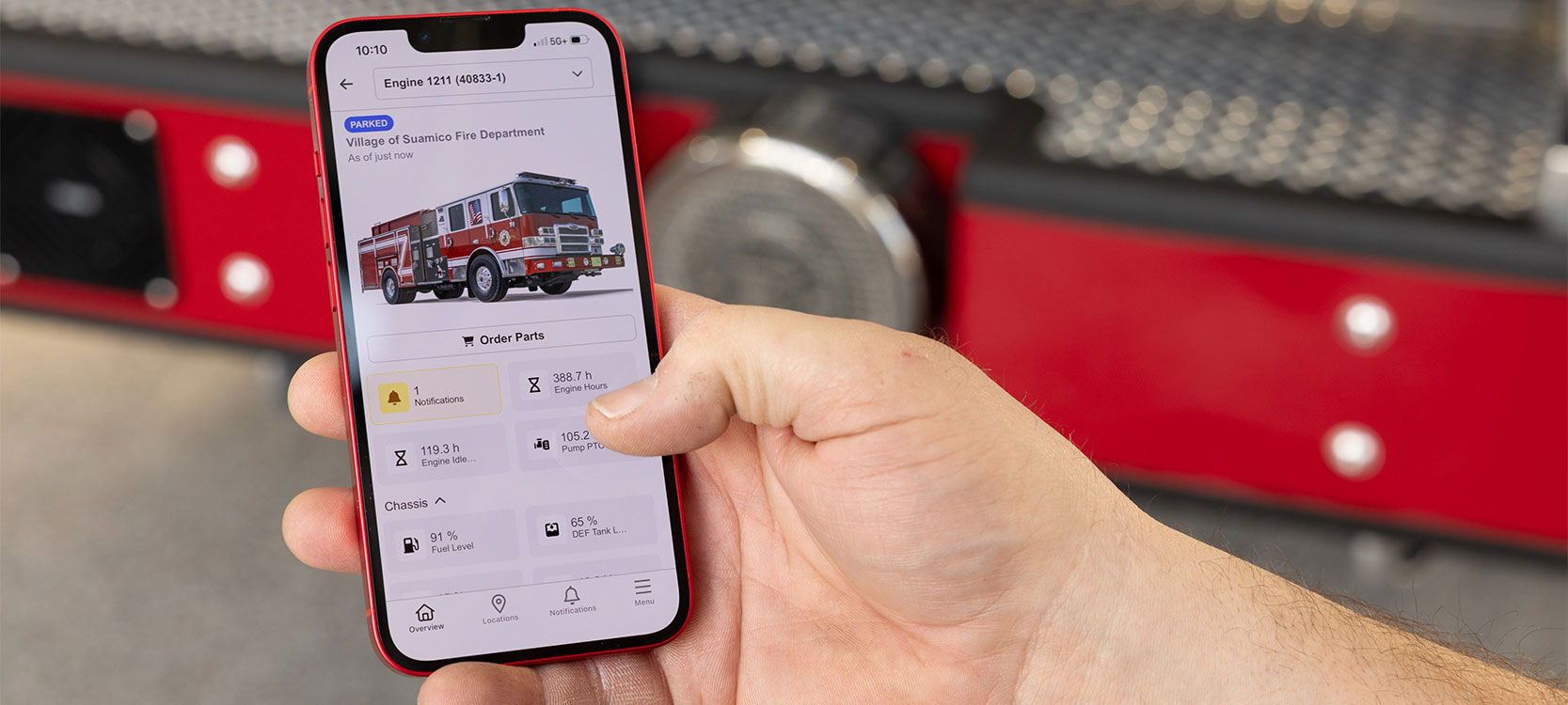 A cell phone with a fire truck and data points on the screen being held in a hand in front of a fire truck bumper.