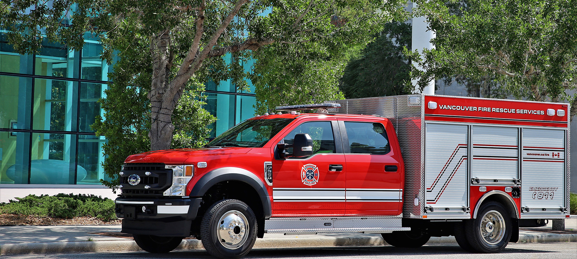 Pierce Ford Commercial fire truck chassis parked outside near a building surrounded by trees. 