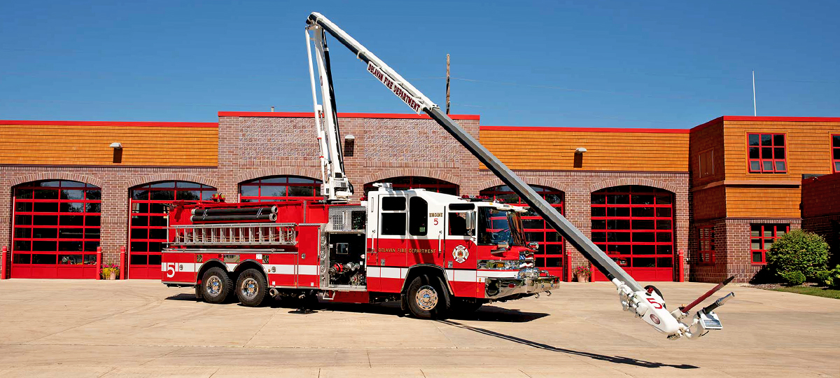 Pierce Fire Truck parked outside on a sunny day in front of a Fire Station with the High-Reach Snozzle extended out in front of the apparatus. 