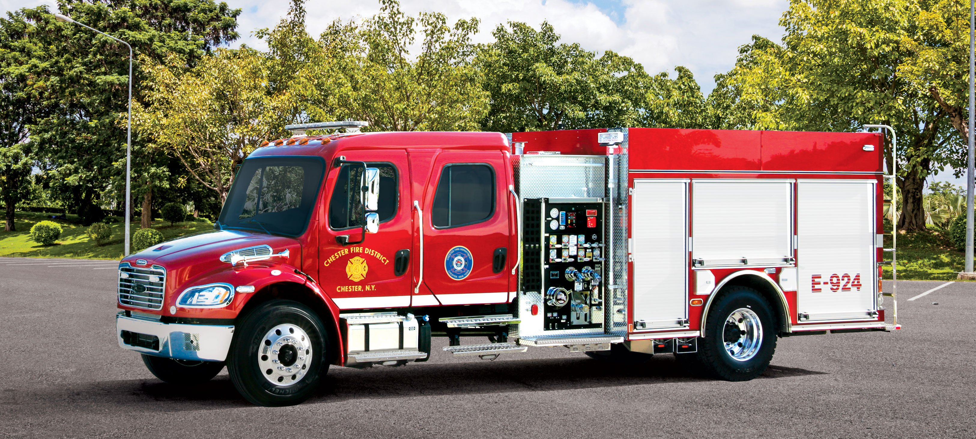 Pierce BX™ Pumper parked outside in a parking lot surrounded by trees on a sunny day. 
