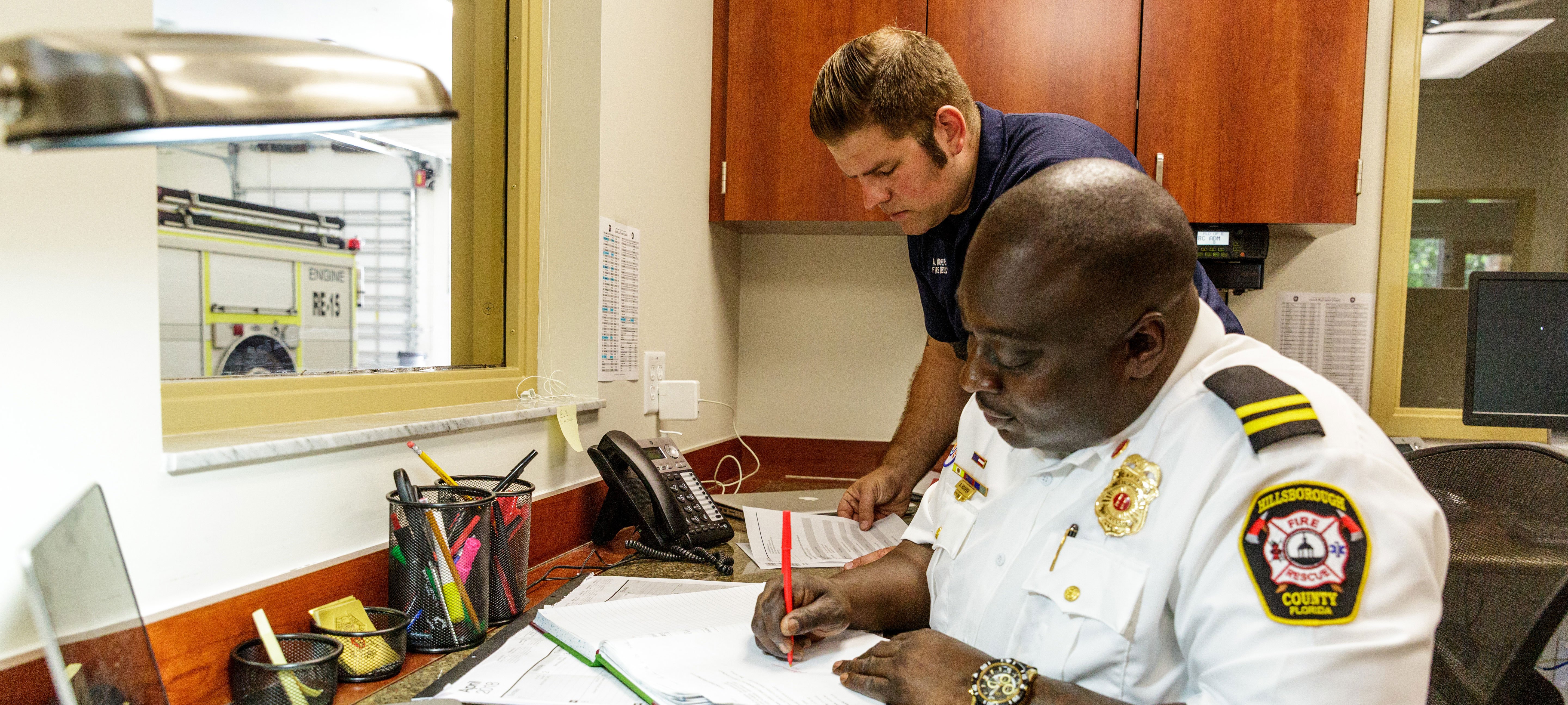 Hillsborough Fire Chief doing paperwork at a desk beside a firefighter in an office. 