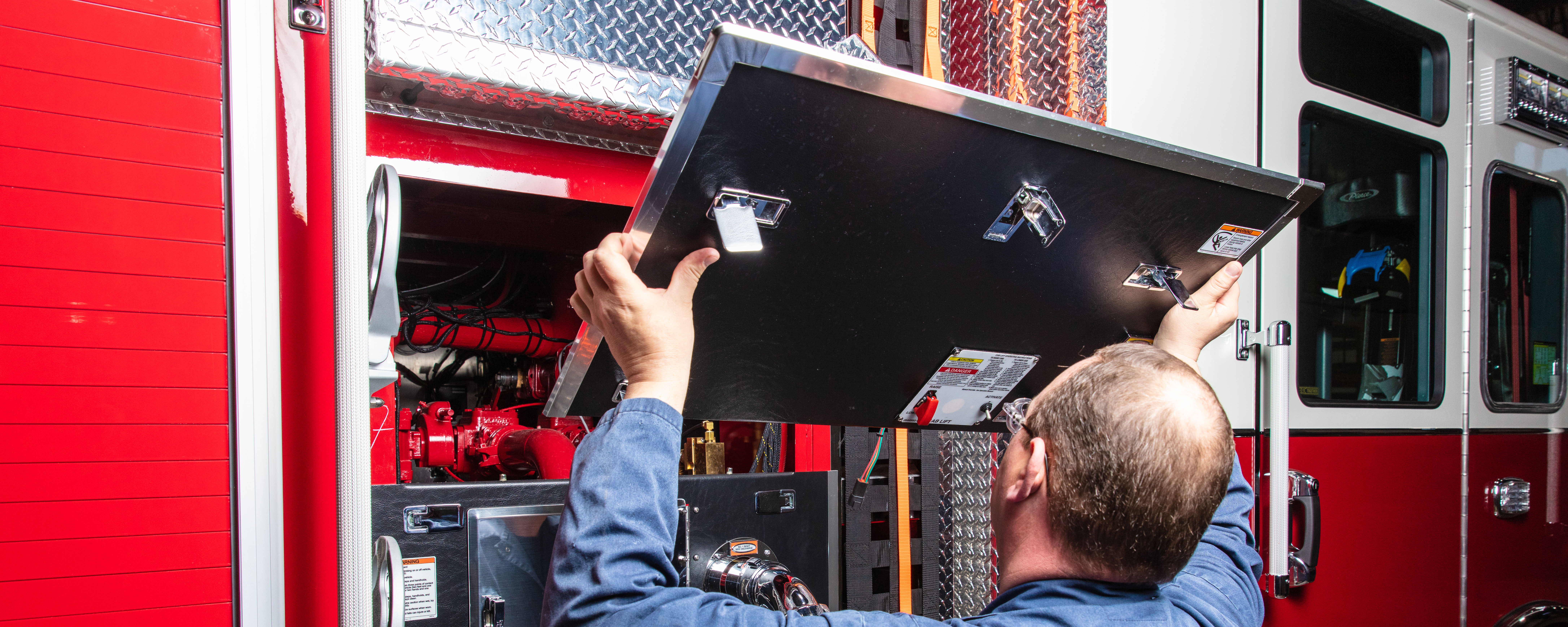 A man removing the door of the pump panel on a Pierce Fire Truck. 