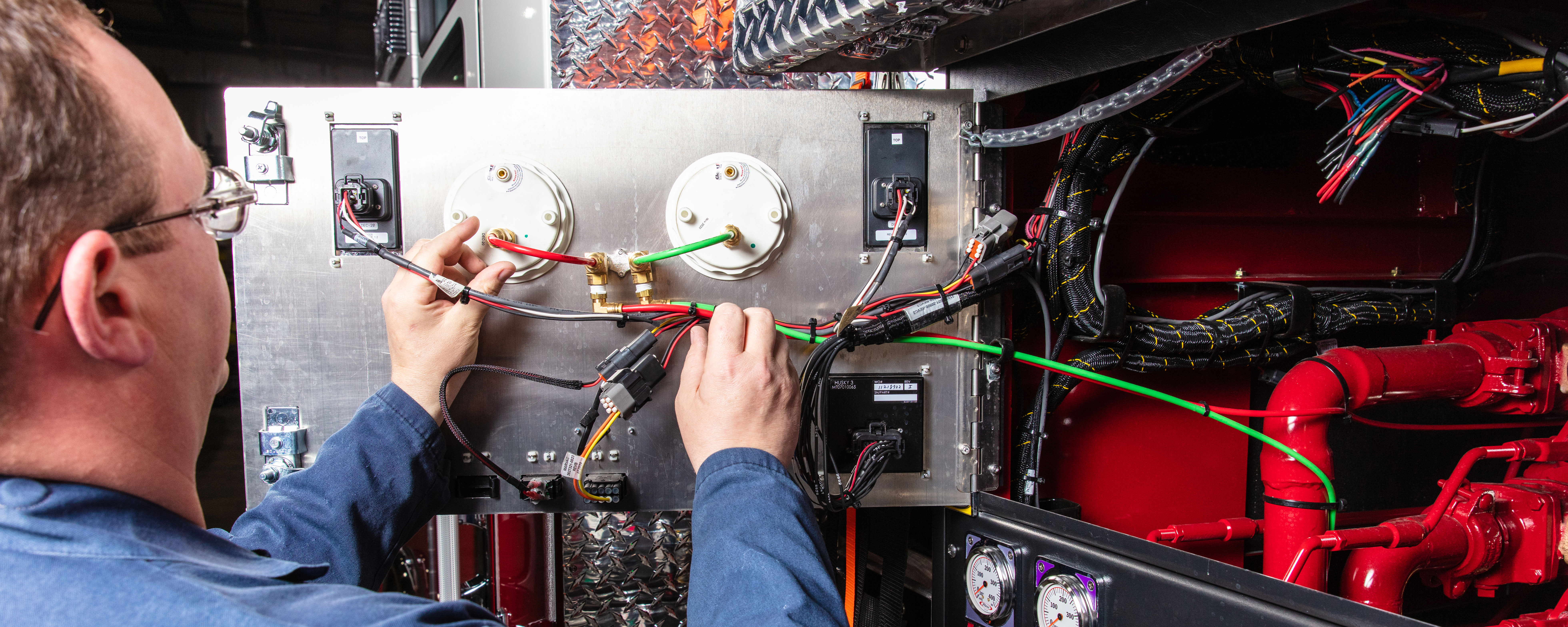 A man servicing the interior configuration on the pump panel on a Pierce Fire Truck. 