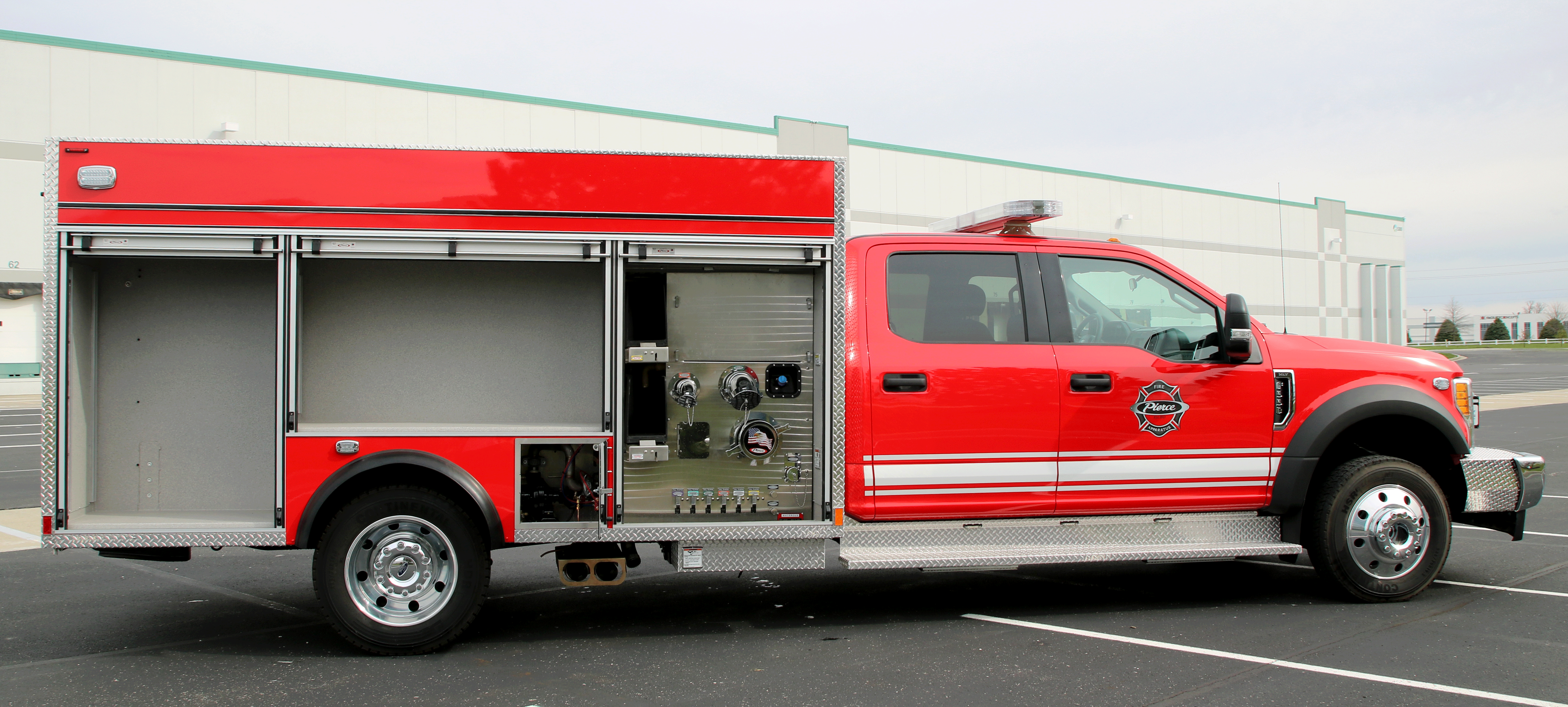 Passenger side of a Pierce Ford commercial fire truck chassis with side compartment doors open to show the storage configuration. 