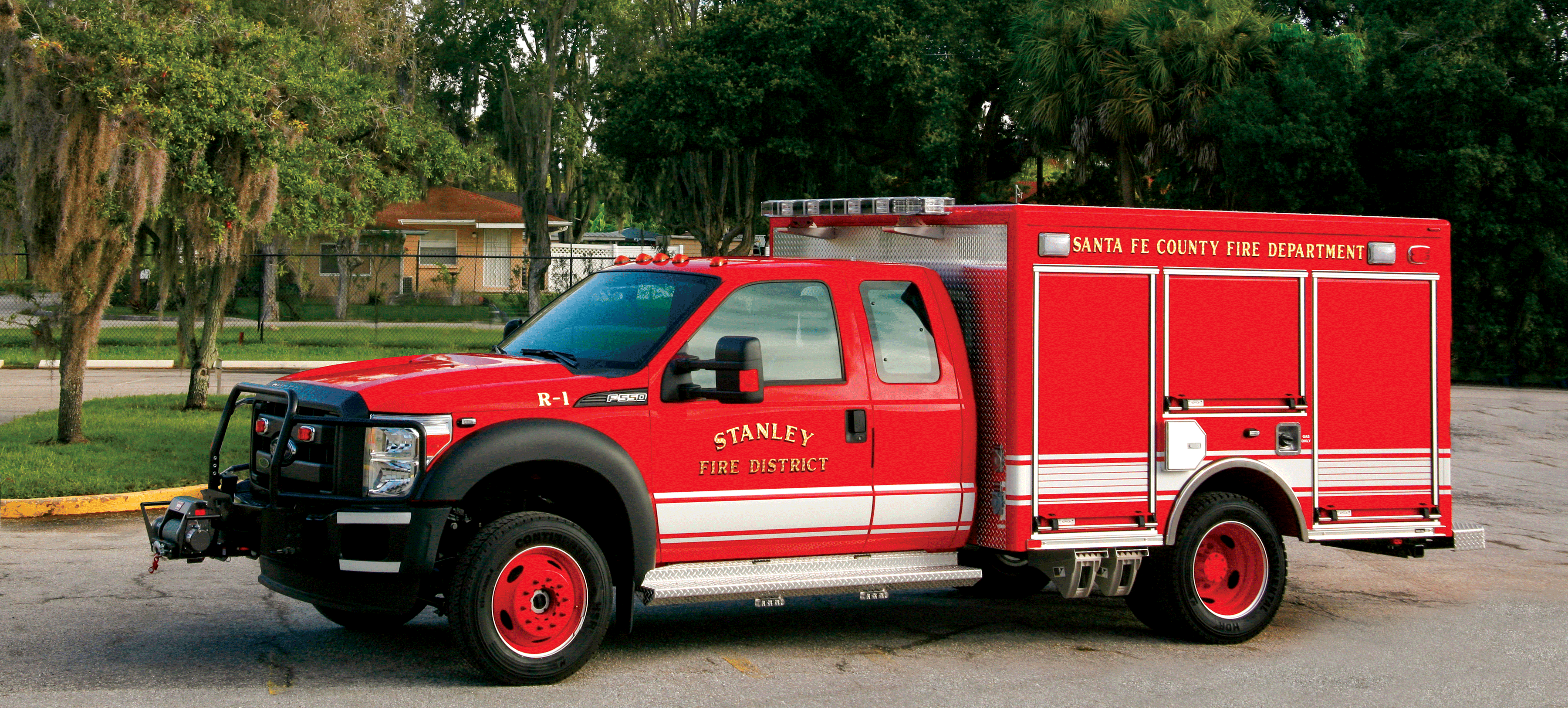 Exterior drivers side of Pierce Ford commercial fire truck chassis parked outside near trees. 